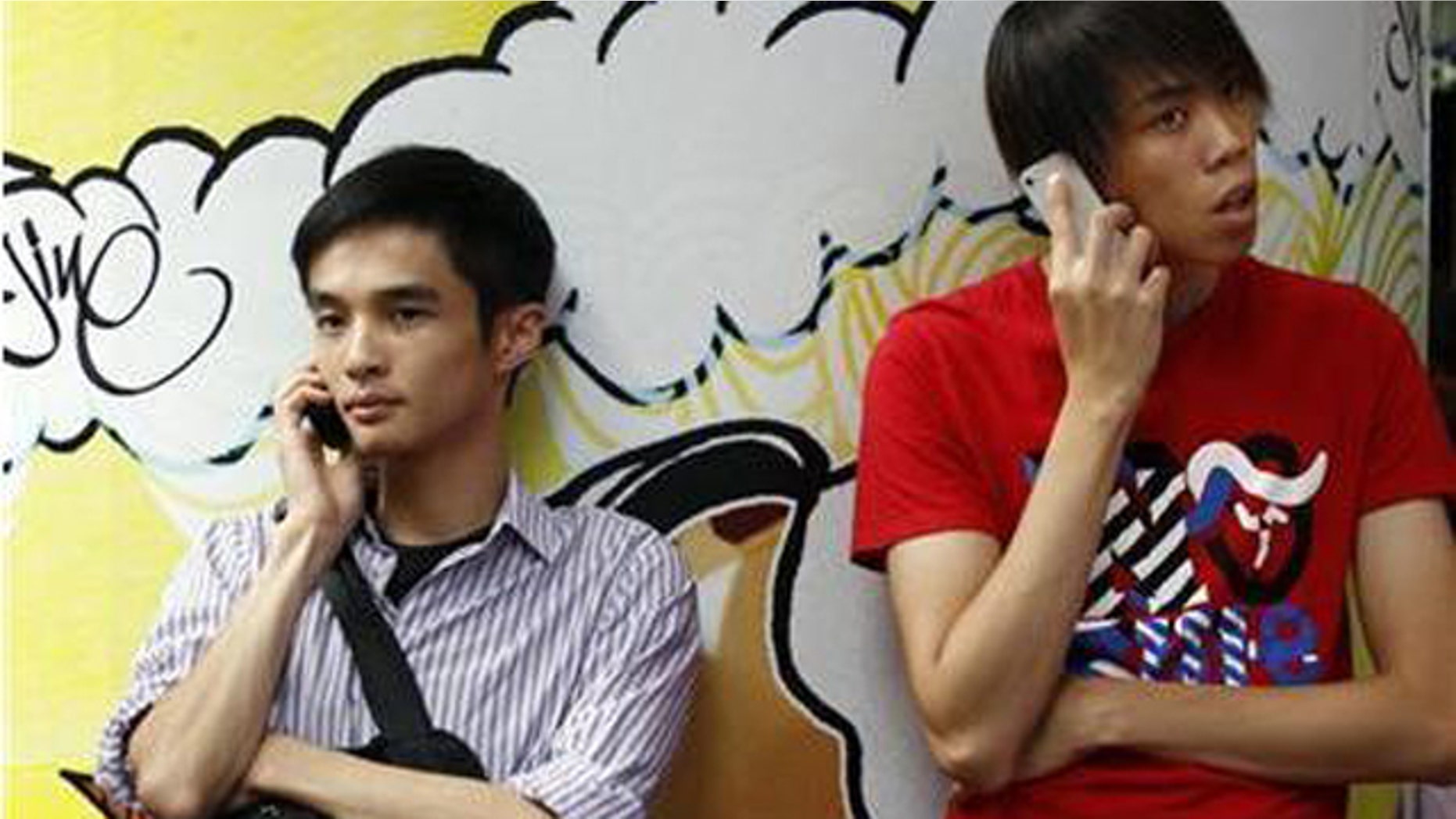 Aug. 16, 2011: Two men use mobile phones as they wait outside a department store in Hong Kong.