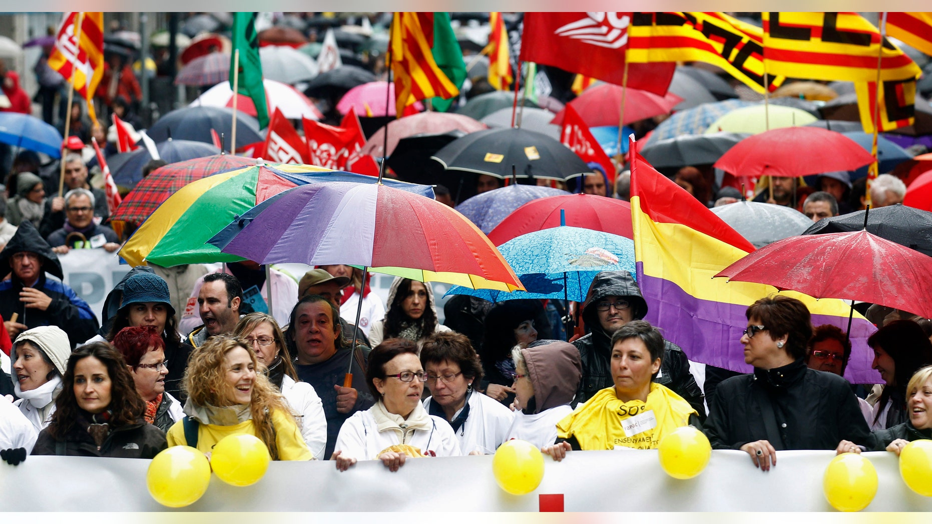 People hold umbrellas as they march with a banner during a protest against government austerity measures in Barcelona.