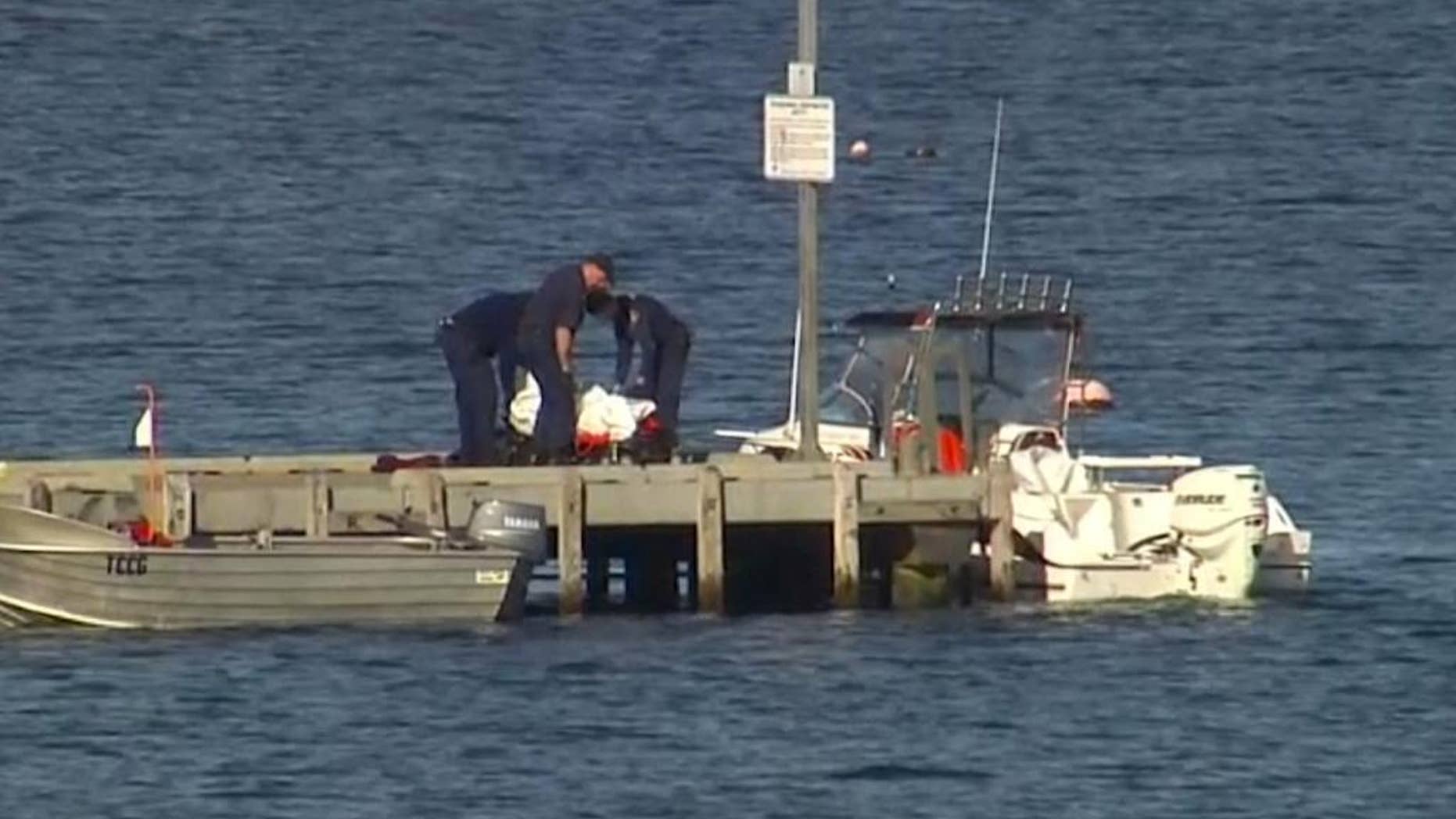In this image taken from video, police carry a body in a bag and place it in on a stretcher on a jetty in Triabunna, off the Australian island state of Tasmania, on Saturday, July 25, 2015. A woman watched her father being mauled to death by a large shark on Saturday while the pair were diving, police said. (AuBC via AP)AUSTRALIA OUT