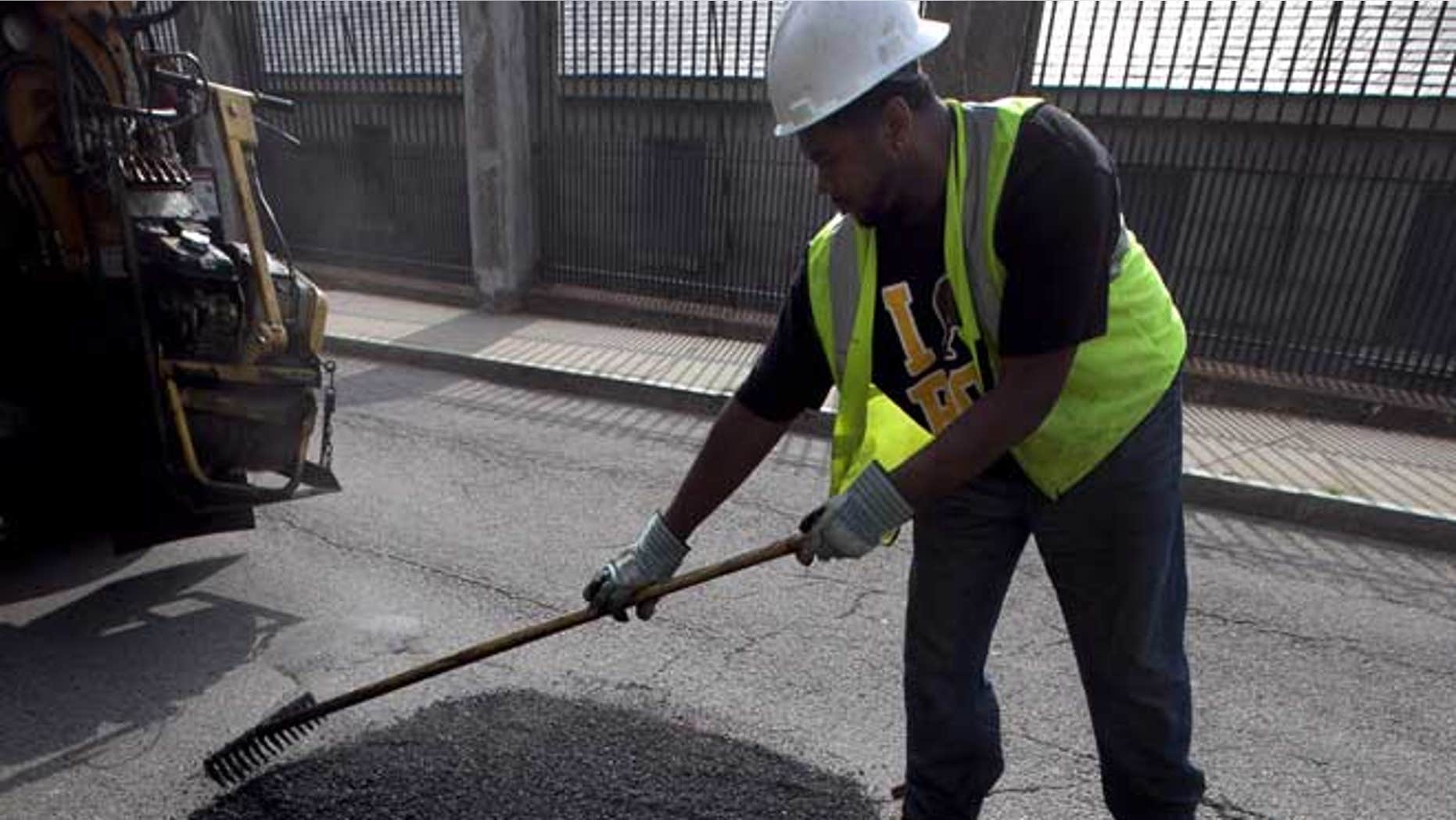In this Thursday, July 19, 2012 photo Boston Public Works worker Tyrone Odom, of Boston, fills a pothole with asphalt in Boston's Charlestown neighborhood.