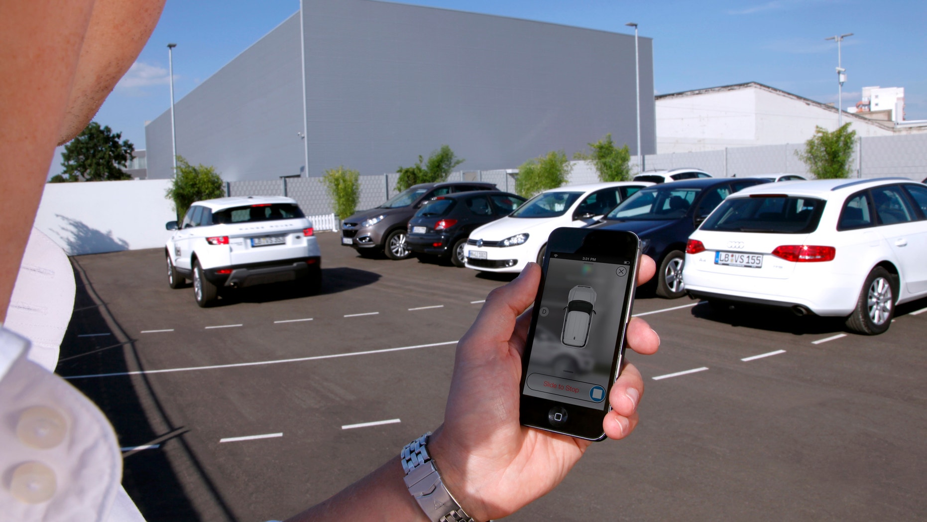In this undated photo supplied by Valeo, a person activates a self-parking vehicle via a smartphone application. Technology being honed by the French auto parts maker uses a dozen ultrasonic sound-wave sensors, 360-degree cameras and a laser scanner to allow a vehicle to safely park within a few centimeters of other vehicles. (AP Photo/Valeo)