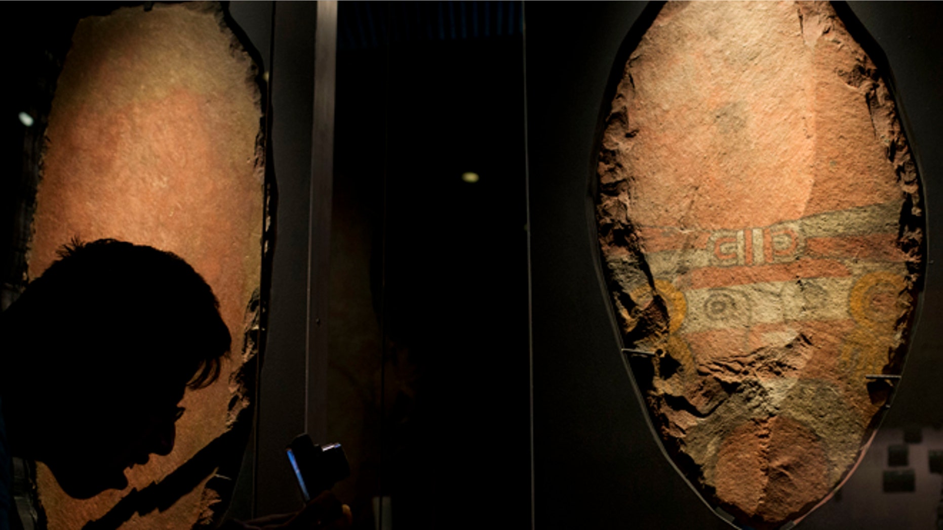 A man bends down to take a picture of a giant, symbolic sacrificial knife, part of a display of items offered to the Aztec god Xochipilli, at the Templo Mayor museum in Mexico City, Friday, Aug. 7, 2015. The Aztecs usually sacrificed quails to Xochipilli, rather than still-beating human hearts. And he was worshipped at vast poetry and music festivals, rather than martial displays. (AP Photo/Rebecca Blackwell)