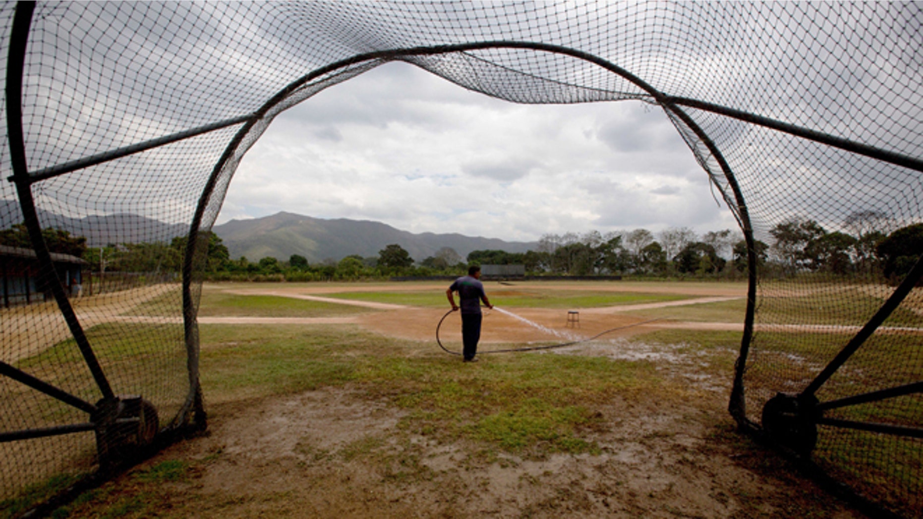 In this March 10, 2015 photo, Seattle Mariners ground worker Carlos Galindez sprays water on the field after a training session at the Seattle Mariners' baseball academy in Aguirre, Venezuela. The teamâs operations are coming to an abrupt end and moving to Dominican Republic, the latest in a string of American teams that have abandoned Venezuela in the past decade as a result of economic turmoil, rampant crime and mounting tensions with the United States. âI donât know why theyâre going,â said Galindez, holding back tears as he reflected proudly on his work caring for the academyâs two baseball diamonds. âAll I can say is they treated us well.â (AP Photo/Fernando Llano)
