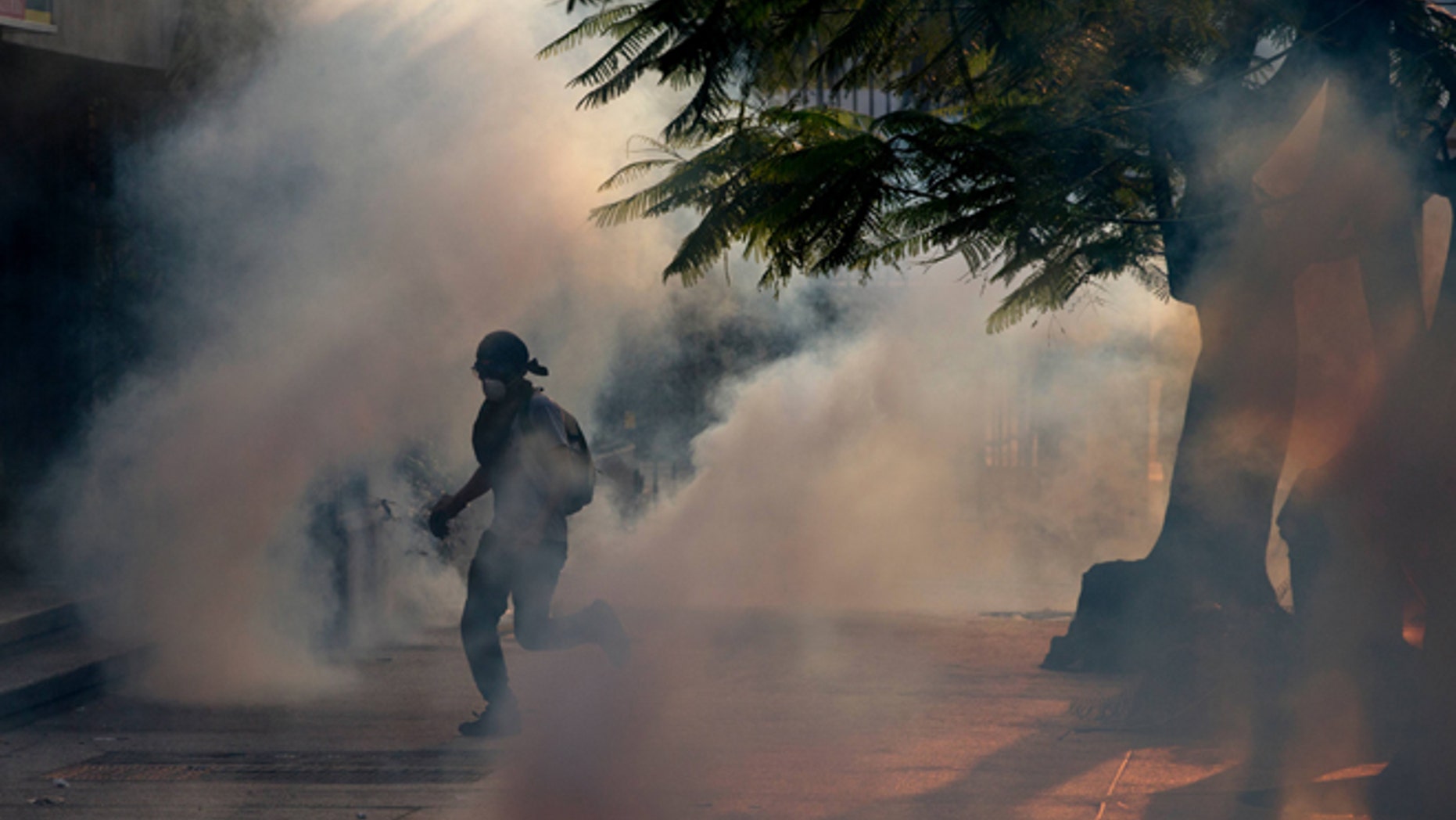 A demonstrator take cover from tear gas fired by Bolivarian National police during clashes with anti-government protesters in Caracas,Venezuela, Saturday, March 8, 2014. The Venezuelan government and opposition appear to have reached a stalemate, in which street protests continue almost daily while the opposition sits out a peace process it calls farcical. (AP Photo/Fernando Llano)