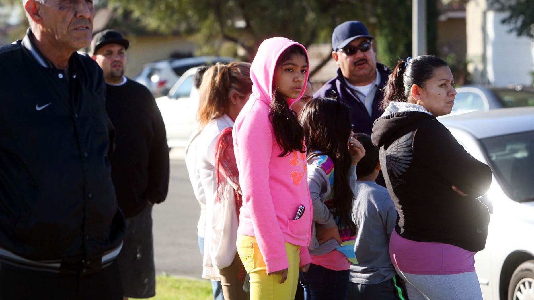 Neighbors look on as police investigate house where a family of four were found shot to death.