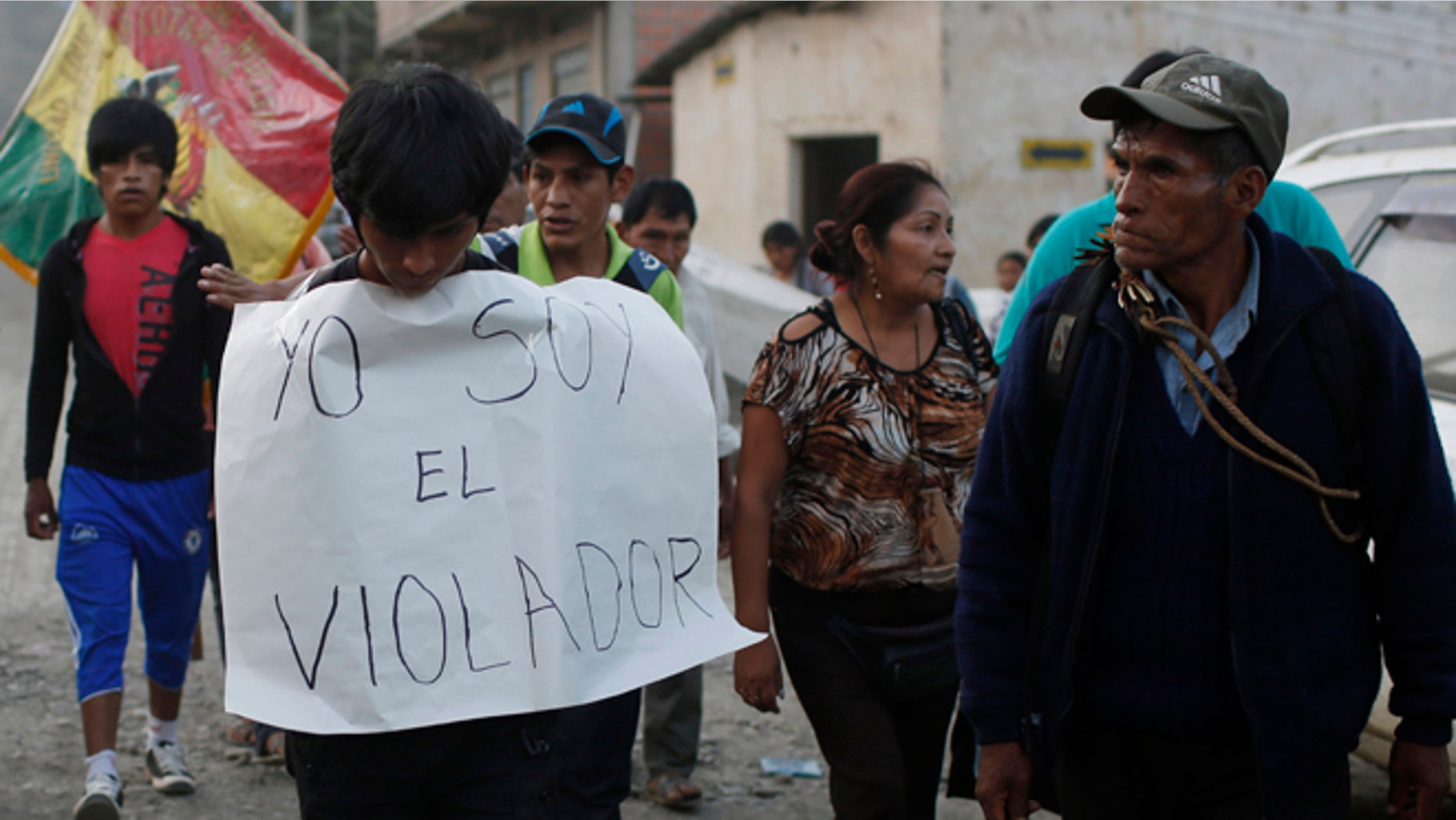 In this June 6, 2015 photo, a man is made to wear a sign with a handwritten message that reads in Spanish; "I'm the rapist," as he is paraded through La Asunta, northeast of La Paz, Bolivia. Groups of citizens patrol the town of 7,000 people, who have imposed a sort of vigilante dry law in the coca-growing mountain town, hoping to end a series of rapes and other crimes. In recent months an 11-year-old girl, and 12-year old girl have been victims of rape in La Asunta, according to local officials. (AP Photo/Juan Karita)