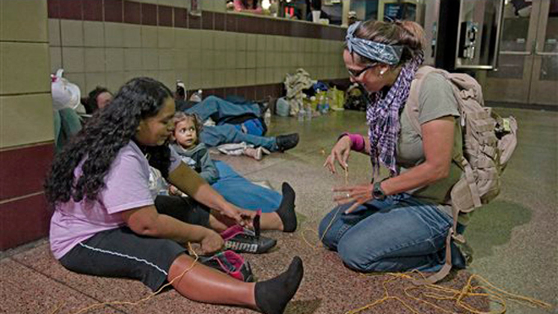 Volunteer Michelle Lewis of Phoenix, right, helps Doris Suyapa, of Honduras, with her shoes, by using yellow rope for shoe laces, Thursday, May 29, 2014 at the Greyhound bus terminal in Phoenix. About 400 mostly Central American women and children caught crossing from Mexico into south Texas were flown to Arizona this weekend after border agents there ran out of space and resources. Officials then dropped hundreds of them off at Phoenix and Tucson Greyhound stations, overwhelming the stations and humanitarian groups who were trying to help. (AP Photo/Rick Scuteri)