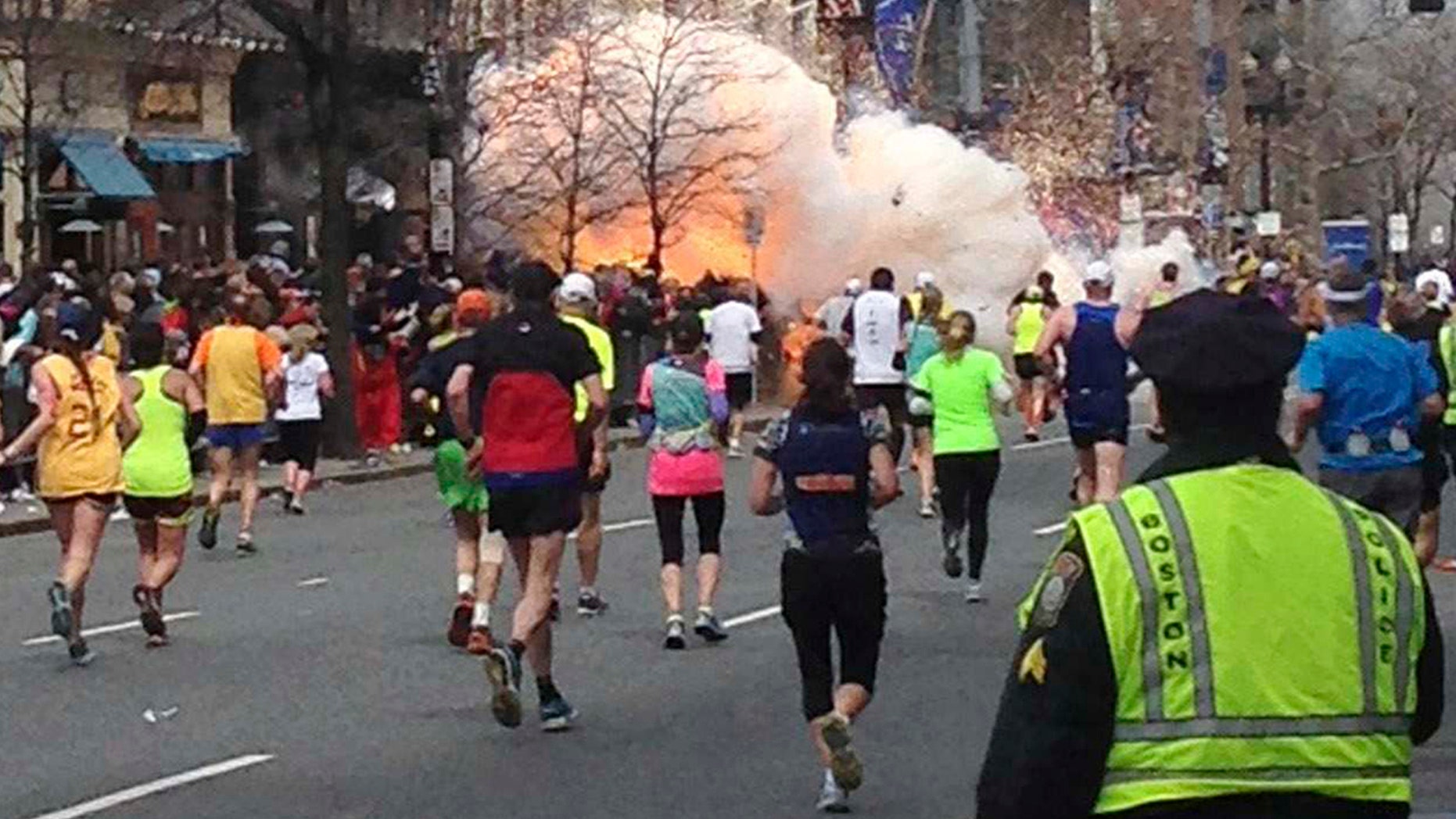 Runners continue to run towards the finish line of the Boston Marathon as an explosion erupts near the finish line of the race. (REUTERS/Dan Lampariello)