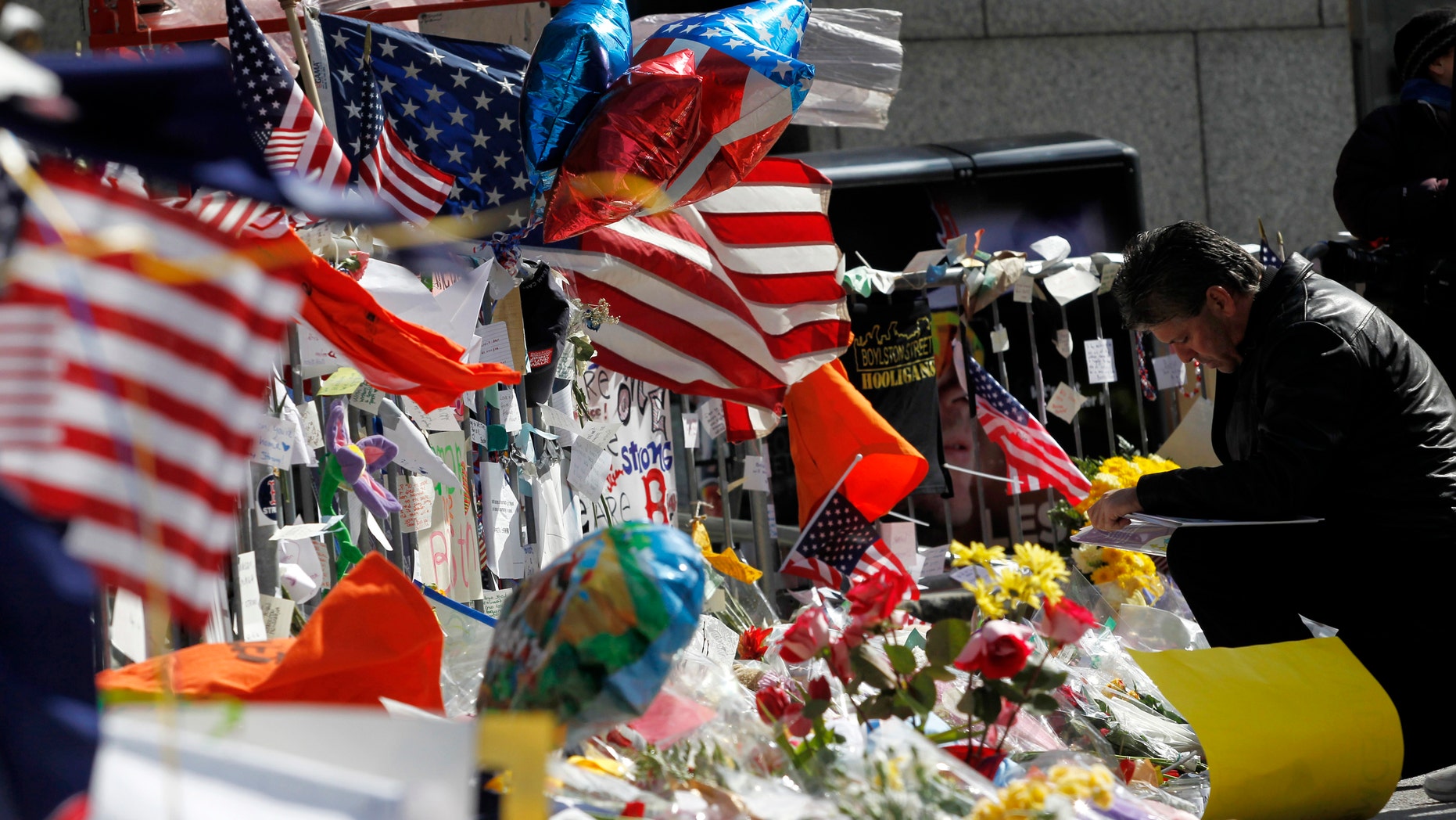 A man kneels down to place a message on a makeshift memorial after observing a moment of silence for the victims of the Boston Marathon bombings marking a week to the day of the bombings at a memorial on Boylston Street in Boston, Massachusetts April 22, 2013.
