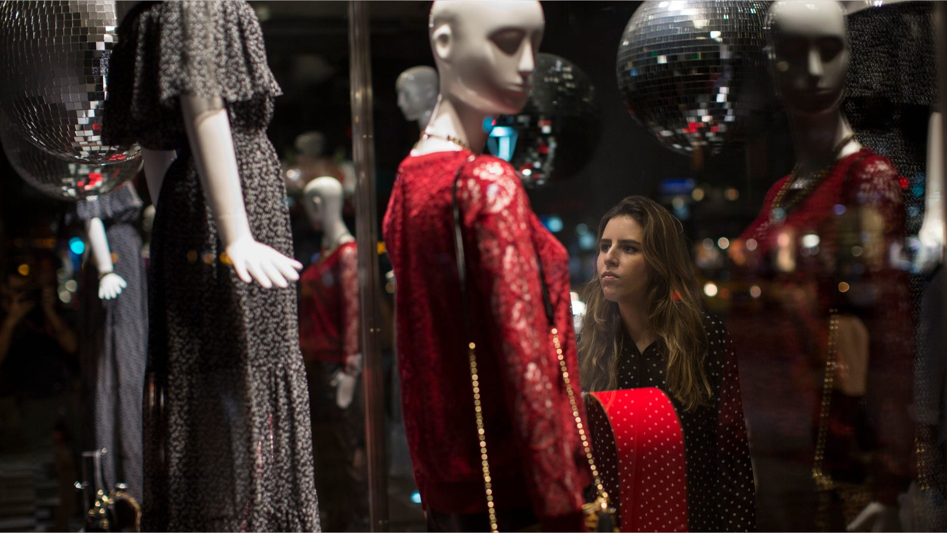 In this Friday, June 12, 2015 photo, a woman is seen through the window of a store as she looks at dresses for sale in Rio de Janeiro, Brazil. Brazilâs top credit information bureaus estimate that as of April, more than 55 million Brazilians were behind on paying off credit cards or loans. Thatâs 37 percent of the adult population in a country of about 200 million people, and the numbers are rising. (AP Photo/Felipe Dana)