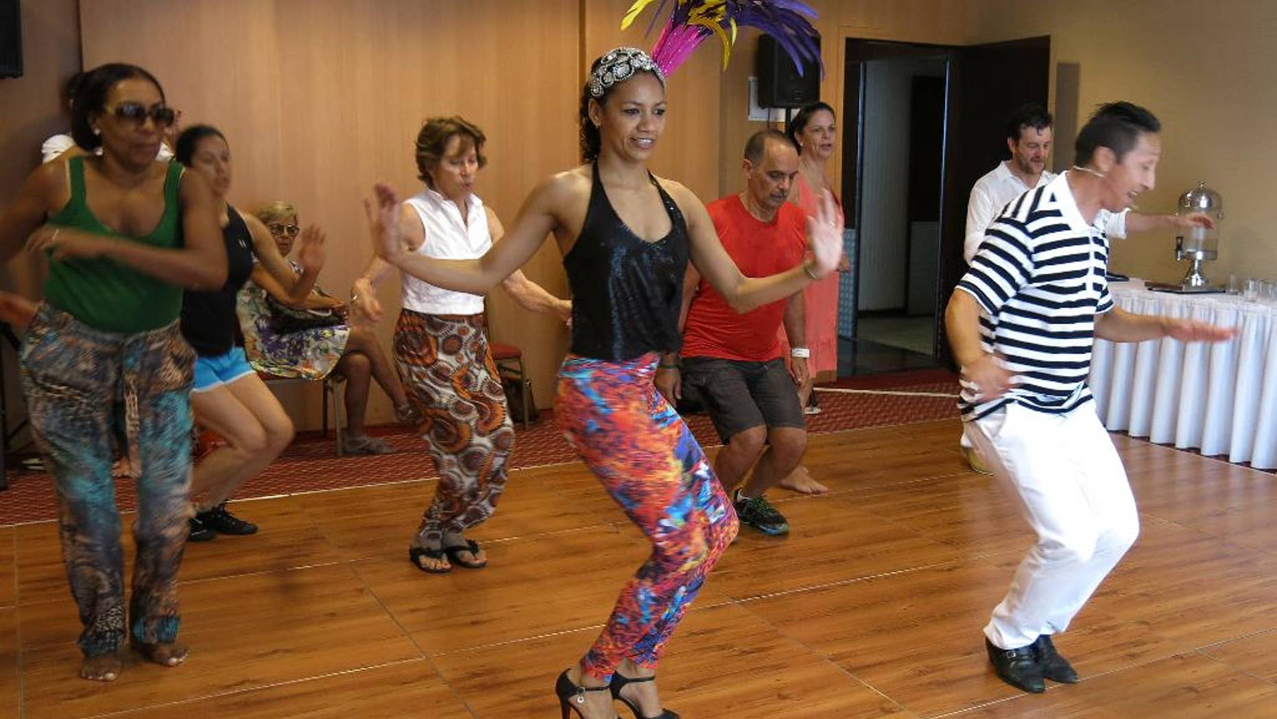 Nete Vieira, center, and her husband Naldi, right, teach samba to foreigners in Rio de Janeiro, Sunday, Feb. 15, 2015. There is a self-deprecating phrase Brazilians with poor dancing skills use to explain their awkwardness at the parades during Carnival: I samba like a foreigner. But even foreigners visiting Brazil for Carnival celebrations can learn a few basic moves thanks to the patience of dancing duo Nete Vieira and her husband Naldi. They teach the basics of rhythmic bouncing, marching and arm waving that will help newcomers have fun, and feel less intimidated, while joining the raucous parties that crowd the streets of Rio de Janeiro. (AP Photo/Adriana Gomez)