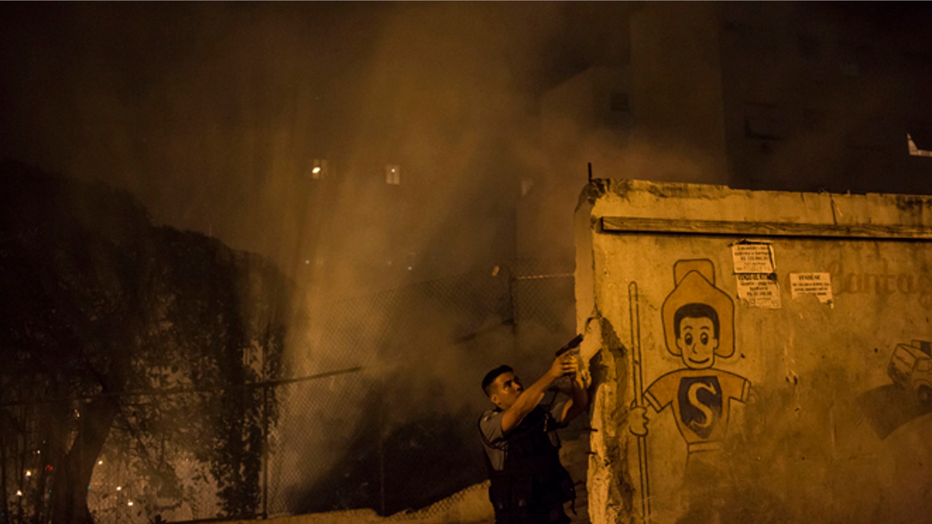 A Police officer of the Pacifying Police Unit, patrols among the smoke from burning barricades during clashes at the Pavao Pavaozinho slum in Rio de Janeiro, Brazil, Tuesday, April 22, 2014. Intense exchanges of gunfire, numerous blazes set alit and a shower of homemade explosives and glass bottles onto a busy avenue in Rio de Janeiros main tourist zone erupted Tuesday night after the death of a popular young shantytown resident. (AP Photo/Felipe Dana)