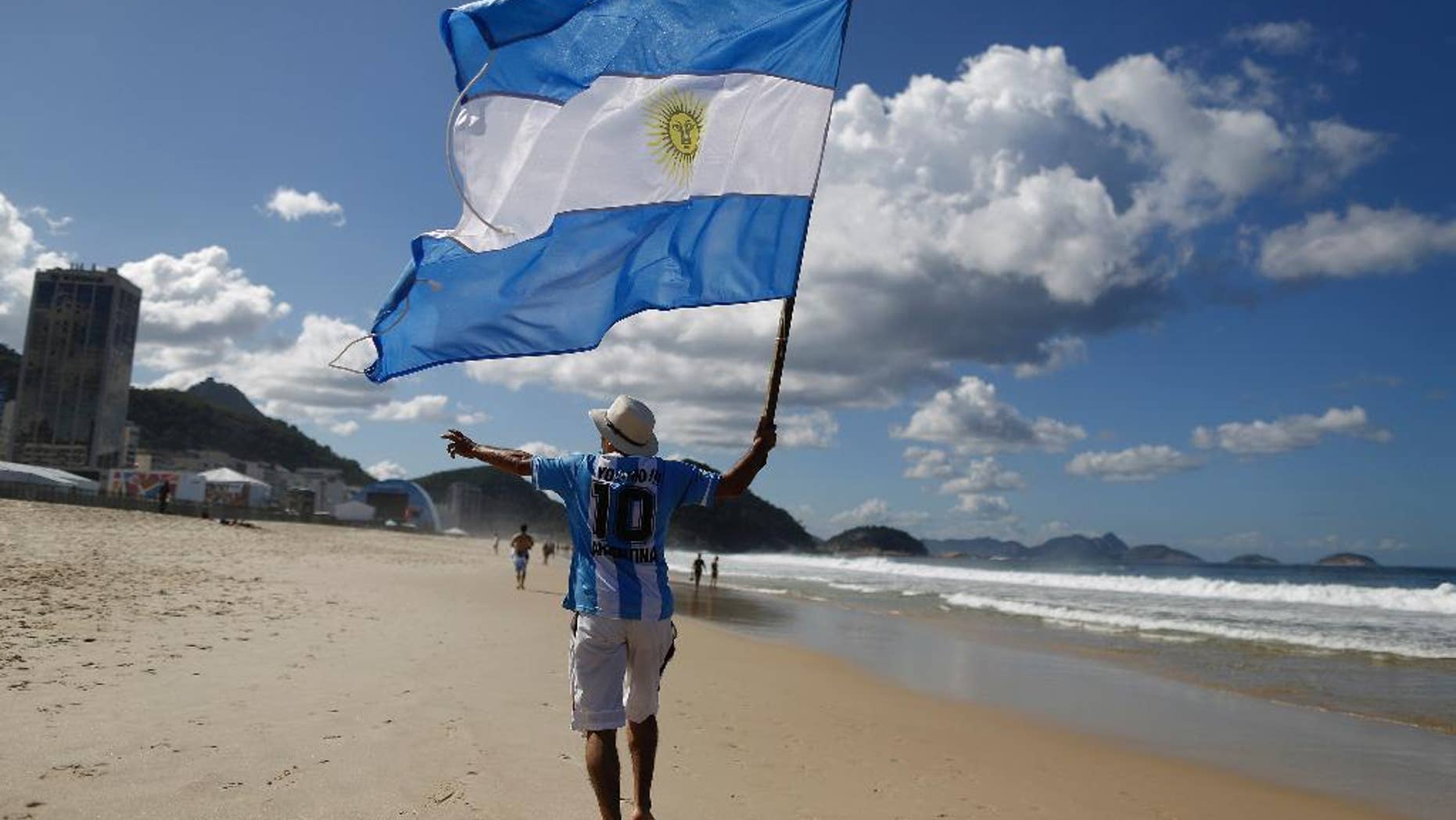 FILE - In this July 14, 2014, file photo, an Argentina soccer fan waves Argentina's national flag the morning after his team was defeated by Germany at the World Cup final, on Copacabana beach in Rio de Janeiro, Brazil. Local media reports say tens of thousands of Argentine fans have remained in the country after the tournament ended. But the prospect of a large number of foreigners selling handicrafts, juggling at intersections for handouts or relying on government social services for poor Brazilians has officials worried. (AP Photo/Leo Correa, File)