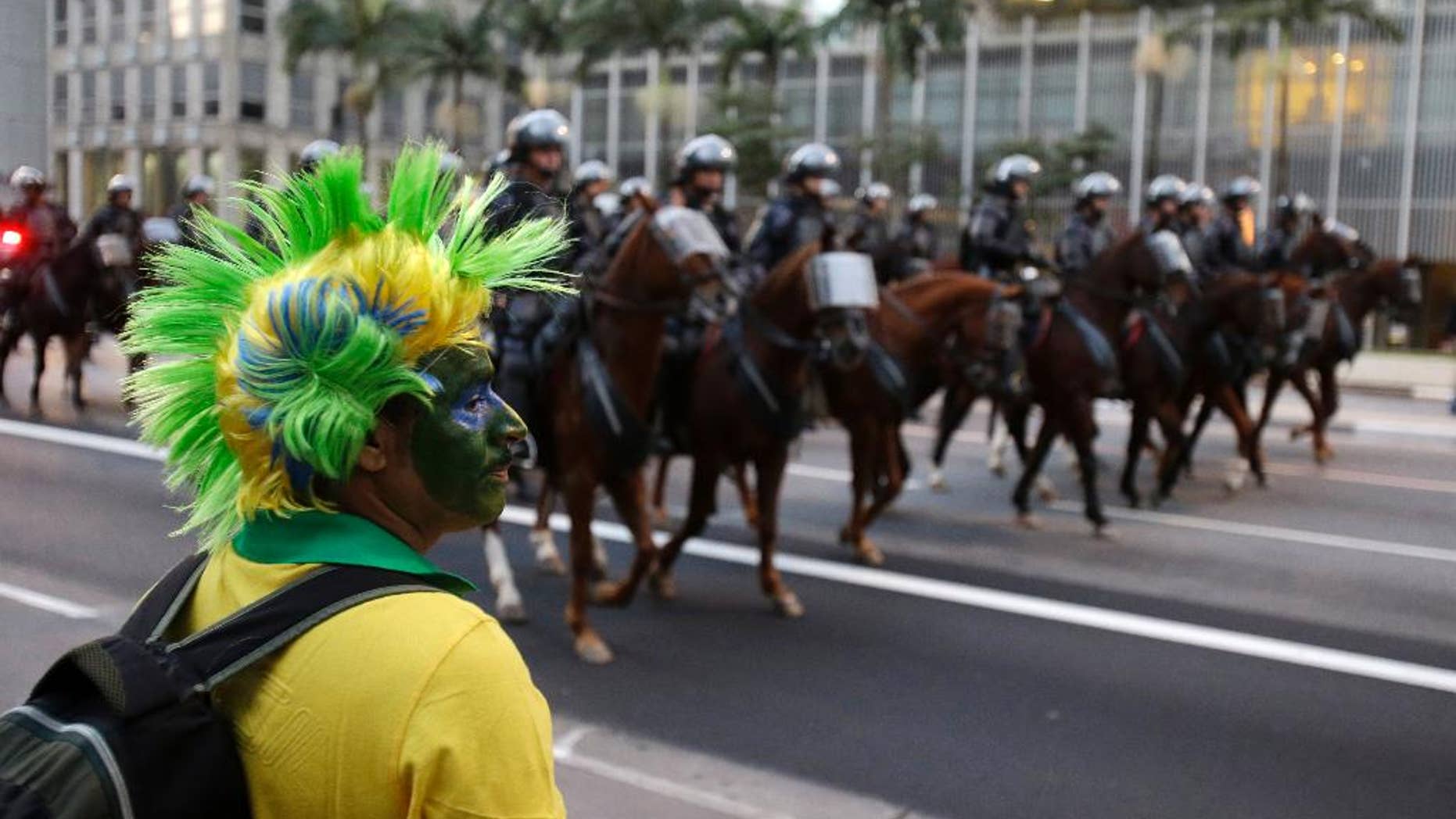A Brazilian fan watches mounted police as they follow about 300 protesters during a rally against the soccer World Cup in Sao Paulo, Brazil, Monday, June 23, 2014. (AP Photo/Thanassis Stavrakis)