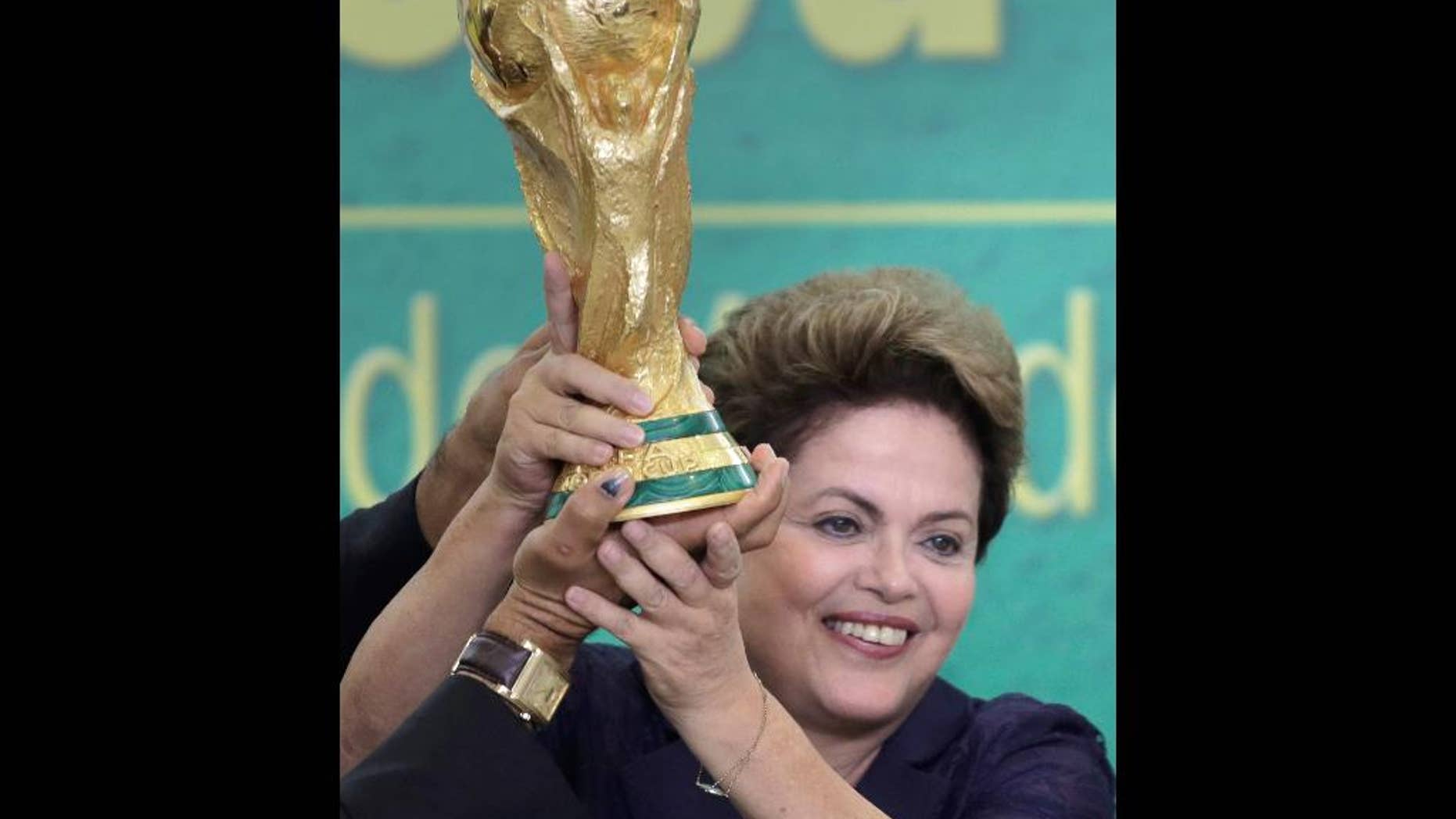 FILE - In this June 2, 2014 file photo, Brazil's President Dilma Rousseff holds up the 2014 World Cup trophy after it was officially presented to Rousseff by FIFA President Sepp Blatter, during a ceremony at the Planalto presidential palace, in Brasilia, Brazil. Rousseff met Friday, July 11, 2014 with a group of foreign journalists in Brasilia, where she hailed Brazil proved skeptics wrong who said the nation couldn't organize a successful World Cup, and said it boded well for its hosting of the 2016 Summer Olympics in Rio de Janeiro. (AP Photo/Eraldo Peres, File)