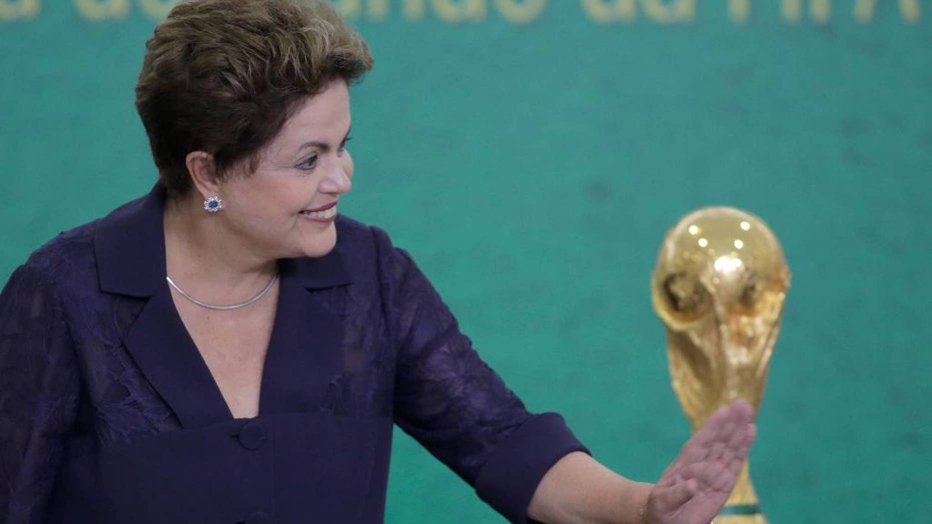 FILE - In this June 2, 2014, file photo, Brazil's President Dilma Rousseff waves to children at a ceremony where FIFA President Sepp Blatter presented the 2014 World Cup trophy to Rousseff at the Planalto presidential palace, in Brasilia, Brazil. President Rousseff has taken to the nation's airwaves Tuesday June 10, 2104, to deliver a pre-taped address trying to rally the nation behind the World Cup that begins this week. (AP Photo/Eraldo Peres,File)