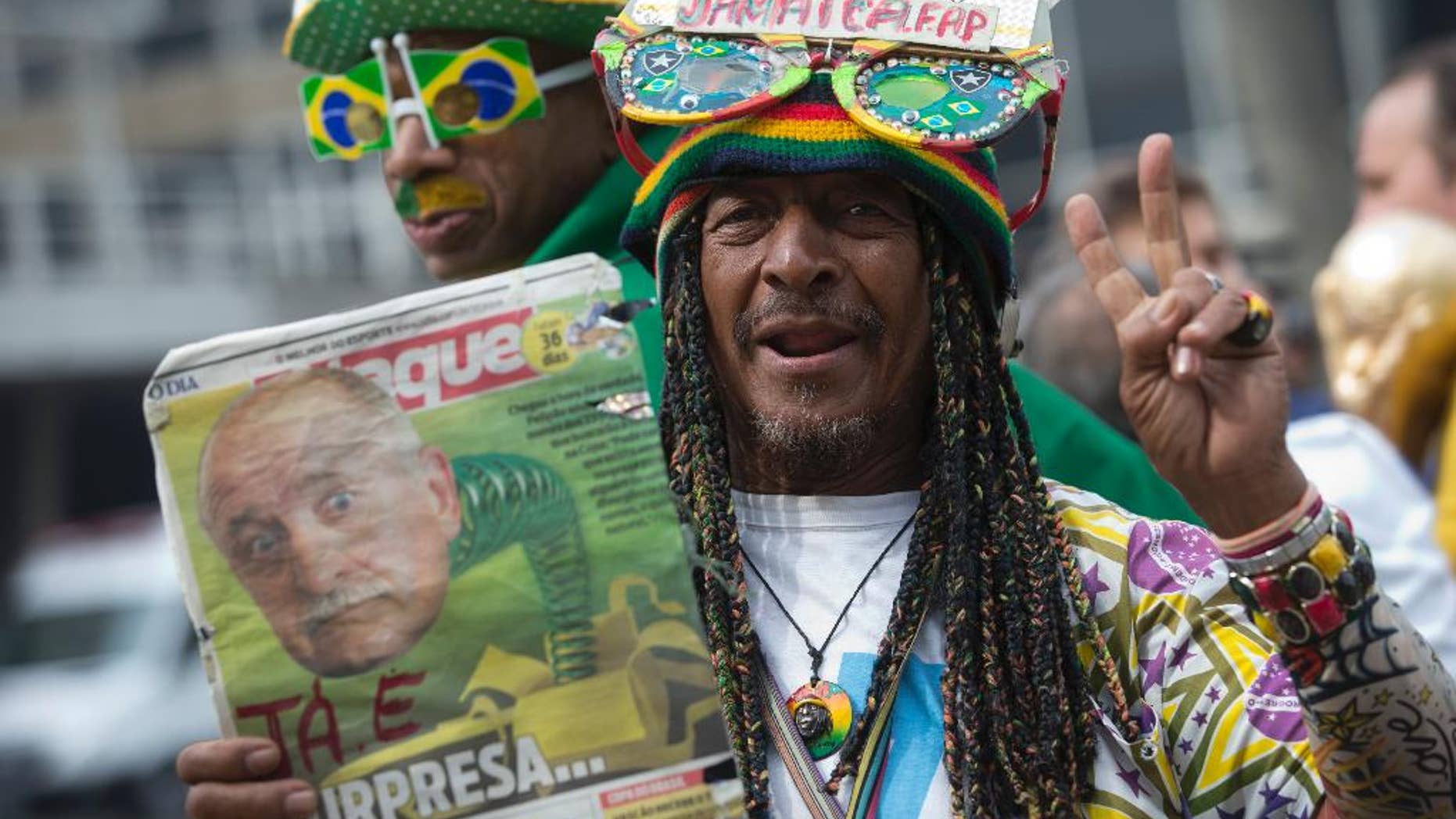 A Brazil soccer fan holds up a newspaper with a photo of Brazil's coach Luiz Felipe Scolari and flashes a victory sign outside the venue where coach Luiz Felipe Scolari is announcing his squad for the upcoming international soccer tournament in Rio de Janeiro, Brazil, Wednesday, May 7, 2014. The team will mix talented young stars such as Neymar and Oscar with more experienced players such as Dani Alves, David Luiz, Thiago Silva and Hulk. Past stars such as Ronaldinho, Kaka and Robinho were left off the squad as expected. (AP Photo/Silvia Izquierdo)