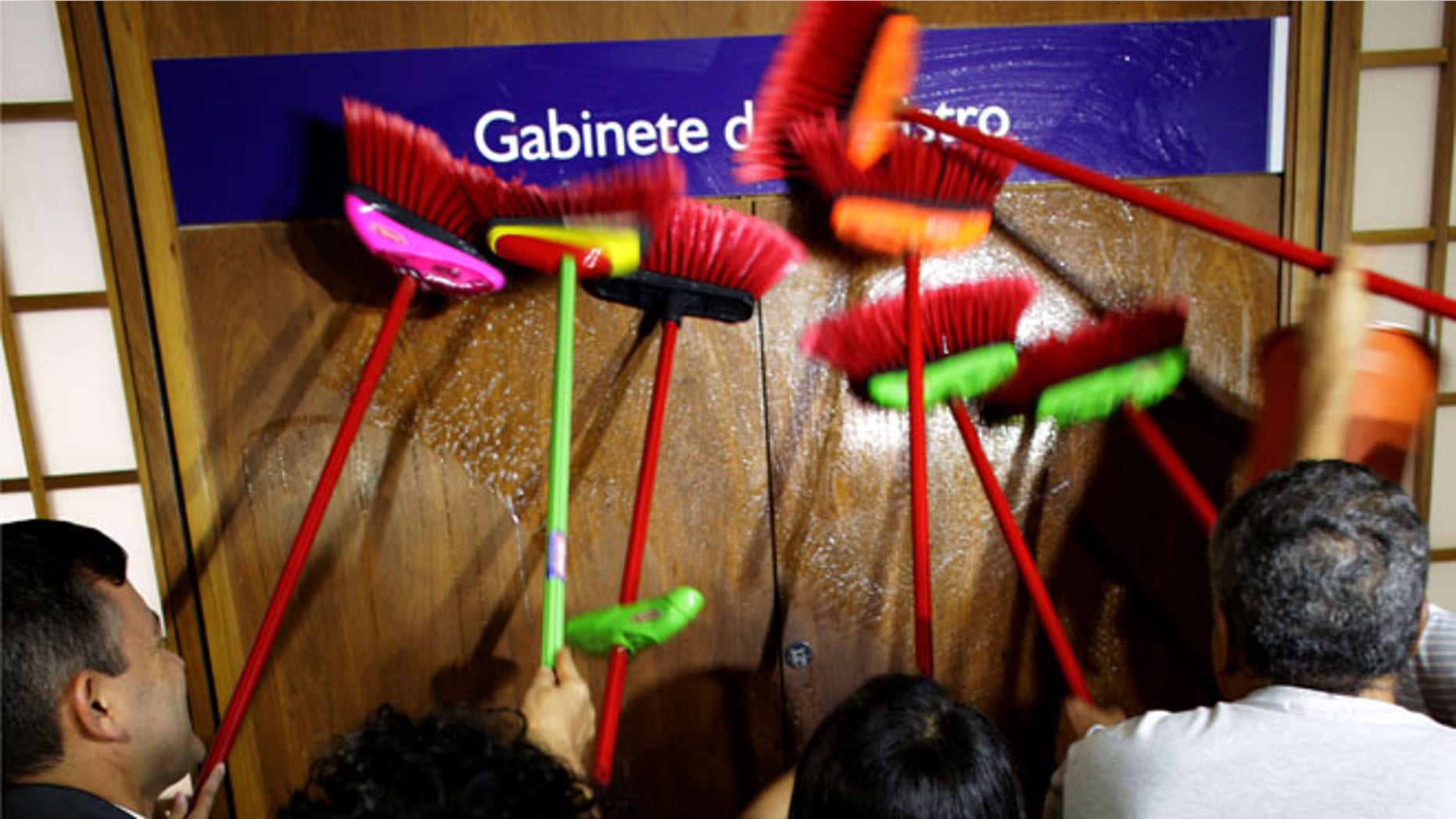 Ministerial staff use brooms to scrub the office door of the Transparency Minister Fabiano Silveira demanding his resignation, in Brasilia, Brazil, Monday, May 30, 2016. A recording TV Globo broadcast late Sunday shows Silveira criticizing Operation Car Wash, a wide-ranging corruption probe of the state oil company Petrobras that has implicated numerous leading Brazilian politicians and businessmen. Protesters in Brazil use brooms as a representation to sweep away corruption. (AP Photo/Eraldo Peres)