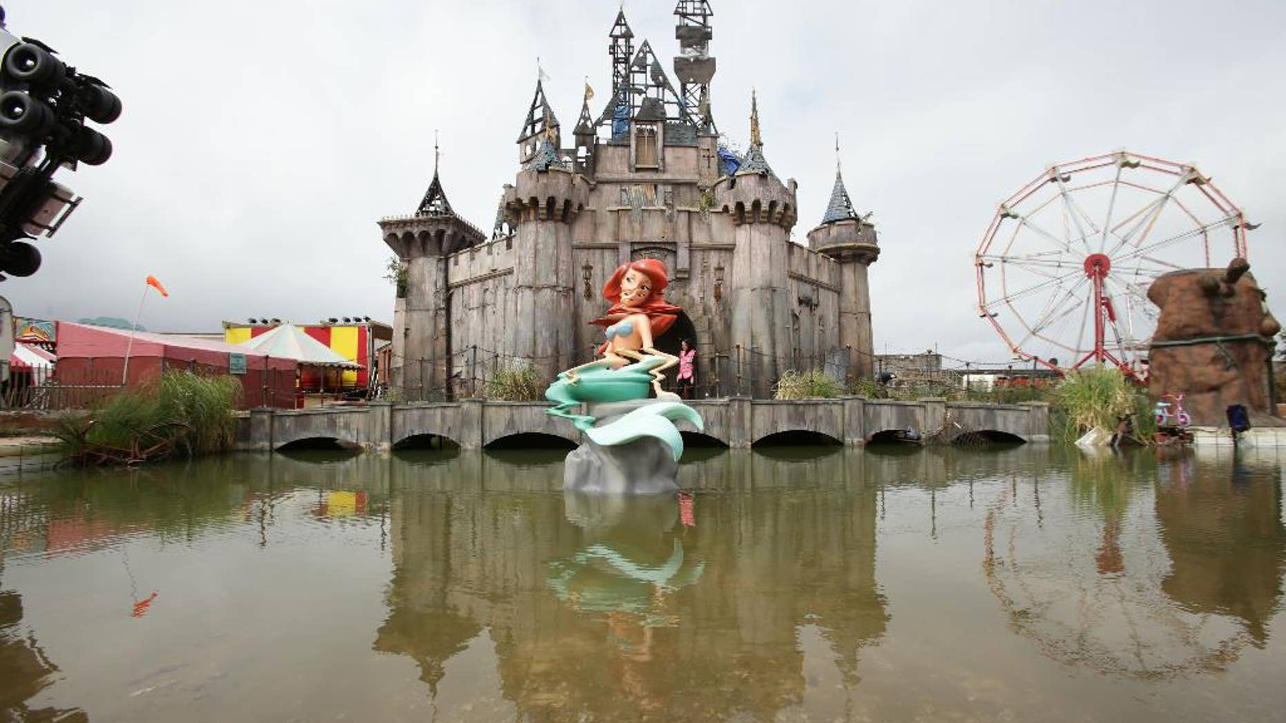 FILE - In this Aug. 20, 2015 file photo, a view of 'Dismaland' , in Western-super-Mare, Somerset, England. An anarchic amusement park by street artist Banksy that mocked capitalism and consumer culture has brought an economic boom to a faded seaside town. Banksy's Dismaland "bemusement park" transformed a derelict outdoor swimming pool in Weston-Super-Mare into a macabre parody of a theme park, complete with a derelict castle, a dead Cinderella and a Grim Reaper in a bumper car. Local officials say the attraction, which closes Sunday, Sept 27, 2015 after five weeks, drew more than 150,000 people to the southwest England town of 75,000. (Yui Mok/PA via AP, File) UNITED KINGDOM OUT