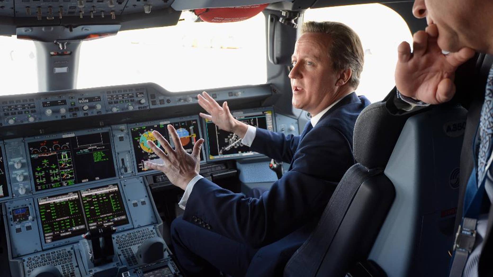 Britain's Prime Minister David Cameron, background, sits in the co-pilots seat, in the cockpit as he is shown around an Airbus A350, during a visit to the 2014 Farnborough Airshow in Hampshire, England, Monday July 14, 2014. (AP Photo/Andrew Matthews, Pool)