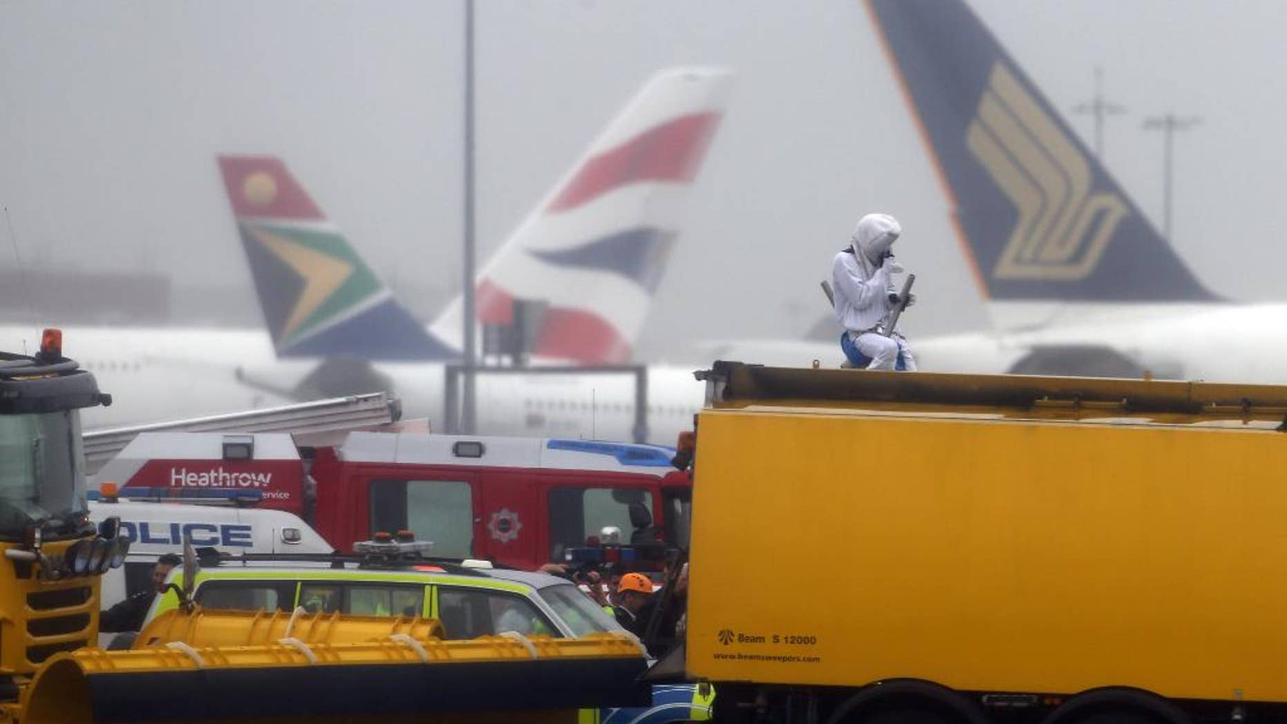 Emergency service workers talk to an activist, dressed as a teddy bear, top right, from the pressure group Plane Stupid, who was one of several demonstrators who occupied the north runway at London's Heathrow Airport to launch a protest Monday July 13, 2015. A spokesman for the action group said a dozen demonstrators cut through a fence and entered the runway early on Monday. (Steve Parsons/PA via AP) UNITED KINGDOM OUT