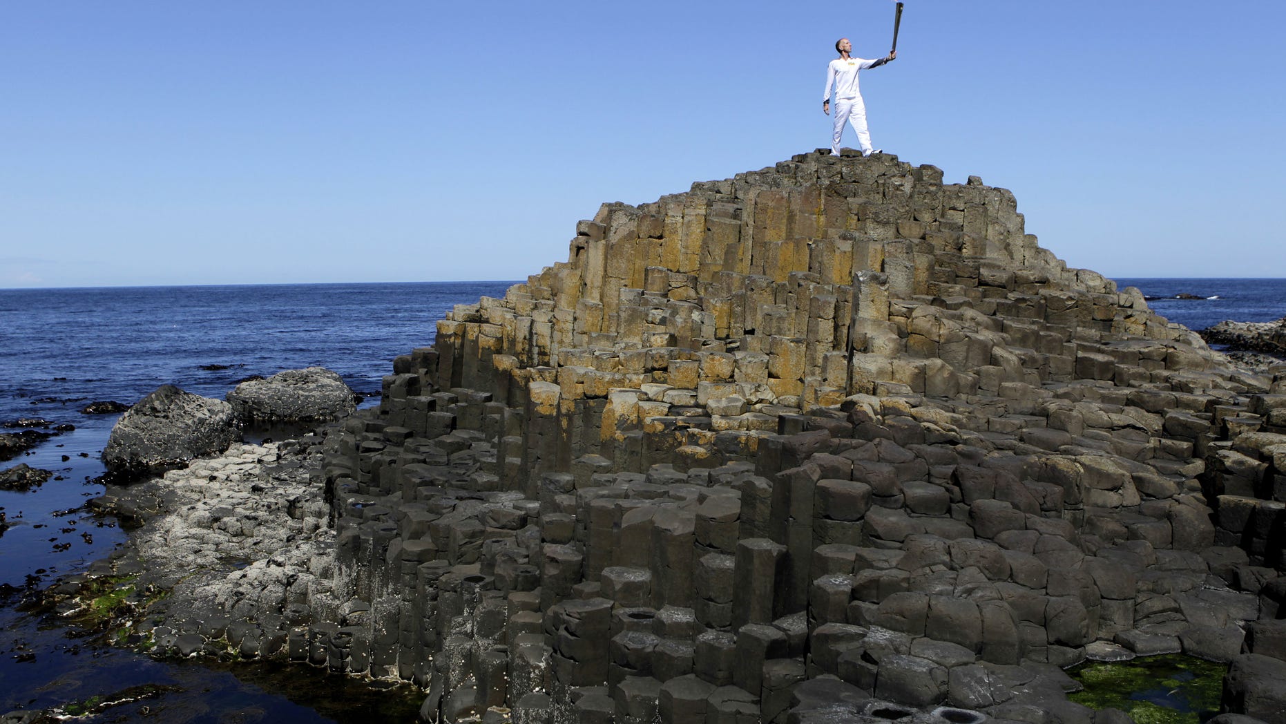 Peter Jack holds the Olympic torch aloft at the Giant's Causeway in county Antrim, Northern Ireland, Monday, June 4, 2012. The Olympic Torch is continuing its relay journey around the country, and is scheduled to arrive at the opening ceremony of the London 2012 Olympic Games. (AP Photo/Peter Morrison)
