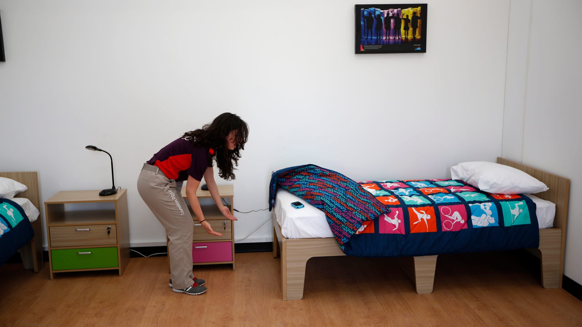 July 12, 2012: An Olympic volunteer shows with her hands an approximation of how much further the length of a standard bed could be extended in length for taller athletes in a display bedroom, that was larger that the real room athletes will have, during a media opportunity at the Olympic and Paralympic athlete's village in London.