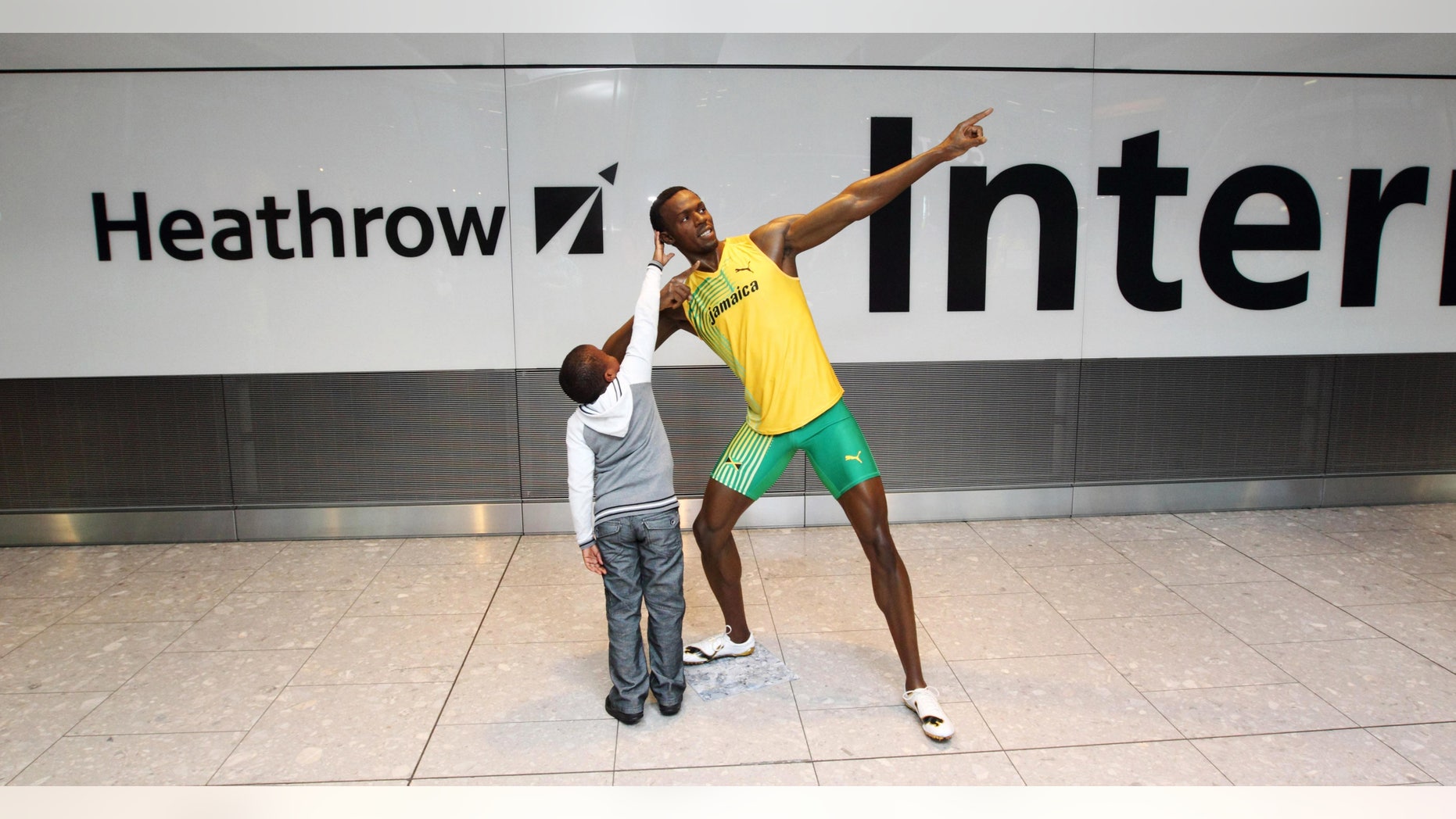 July 12, 2012: A child reaches up to touch the wax figure of Usain Bolt, as passengers arrive at London's Heathrow Airport Terminal 5, are greeted by the wax figure.