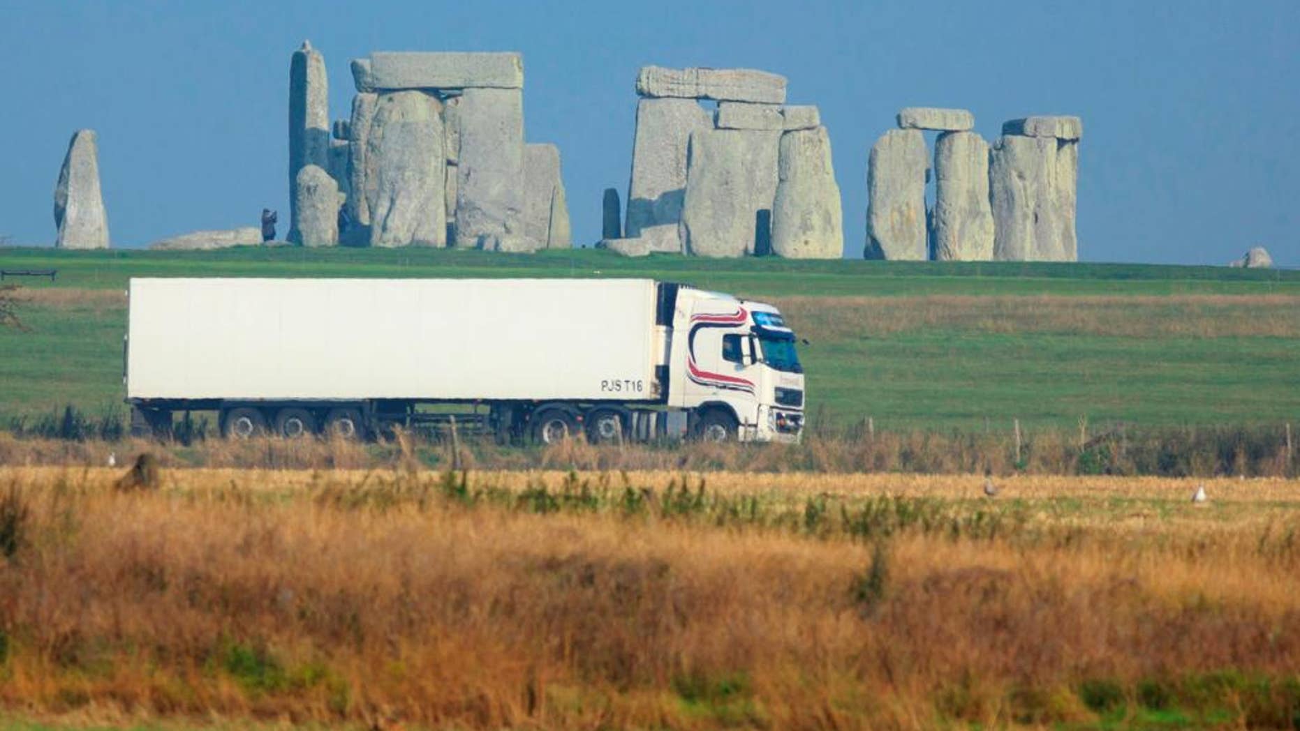 This is an undated handout photo issued by the National Trust, via the Press Associated of a truck passing Stonehenge on the A303 road in Wiltshire England. Visitors to Stonehenge will no longer have to shut out the sound of thundering traffic as they admire ancient monument. The 1.8-mile (2.9 kilometer) tunnel, part of a 2 billion pound ($3.2 billion) upgrade to the road, will eliminate motorists’ view of the stone circle. But Helen Ghosh, director of heritage group the National Trust, said visitors to the site "will once again be able to hear the sounds of skylarks singing rather than the constant noise of traffic." (AP Photo/John Miller/National Trust/PA) UNITED KINGDOM OUT NO SALES NO ARCHIVE
