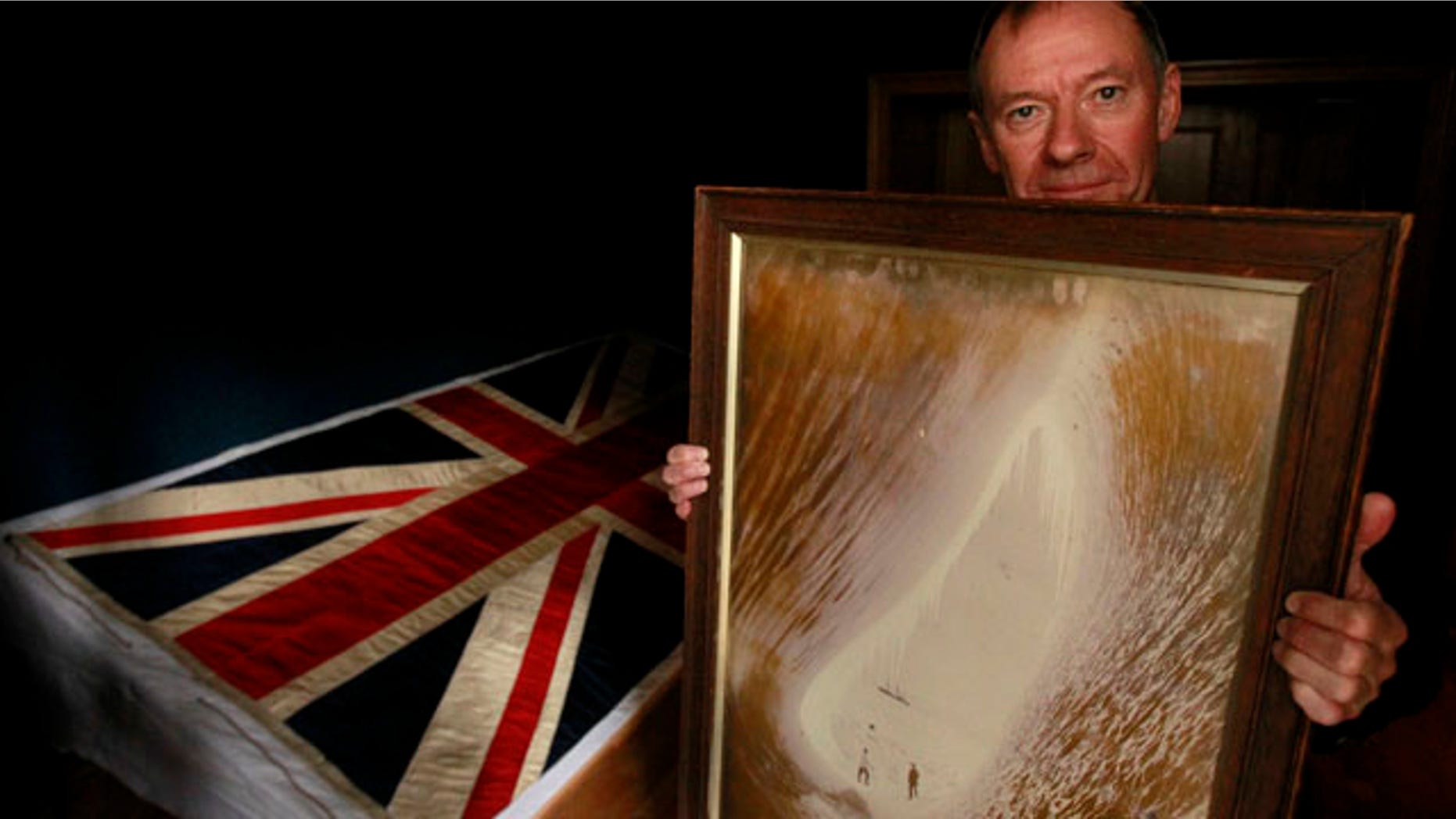 Sept. 20, 2010: Adrian Raeside from Canada, holds a photograph of his grandfather Sir Charles Seymour Wright and great-uncle Thomas Griffith Taylor in front of a silk union flag that belonged to captain Robert Falcon Scott and was used on the two expeditions he led to the Antarctic at the Christie's auction house in London.