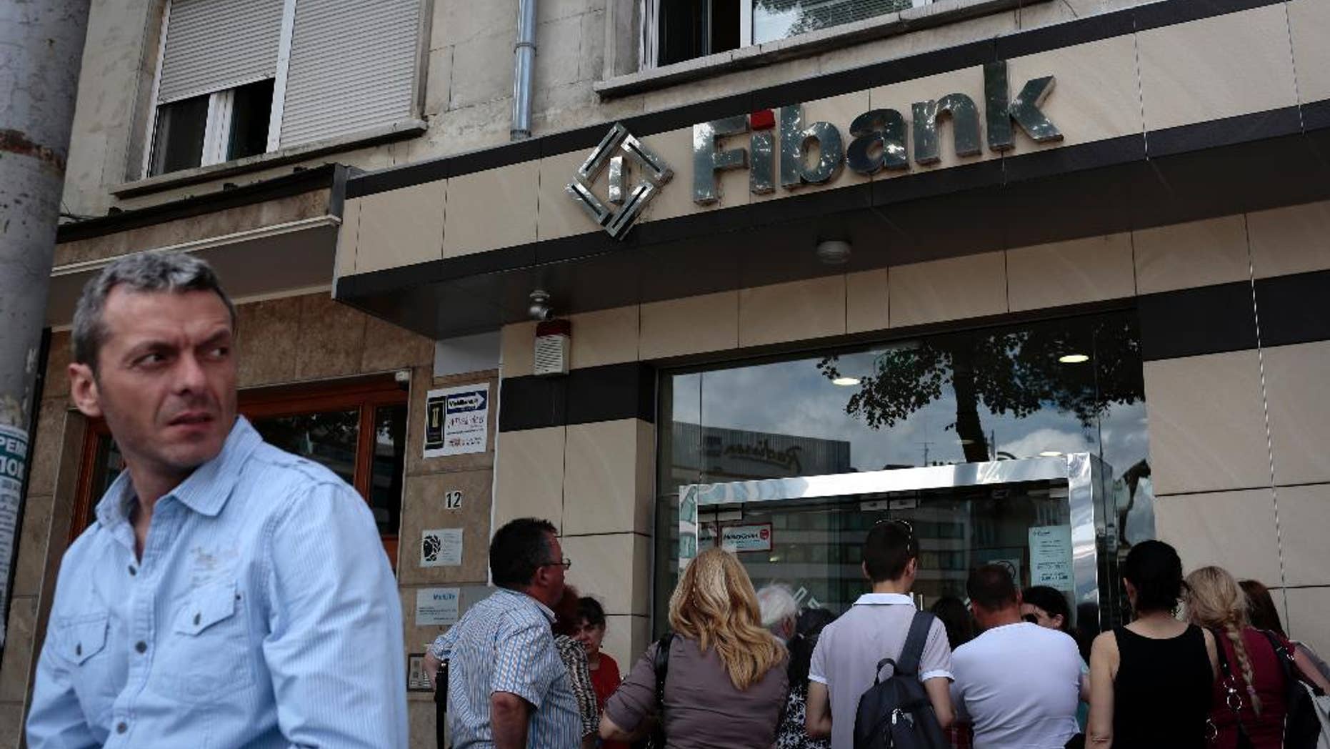 A man stands in front of the a branch of First Investment Bank as people still wait outside at the end of the working time, Sofia, Friday, June 27, 2014. A second Bulgarian bank has been hit by a run within the past week, prompting authorities to issue a statement claiming there is no reason for depositors to worry about their money despite reports the financial system is shaky. First Investment Bank, Bulgaria's third-largest lender, was the target of media rumors on Friday alleging that it was short on liquidity, causing public panic and a run on deposits. (AP Photo/Valentina Petrova)