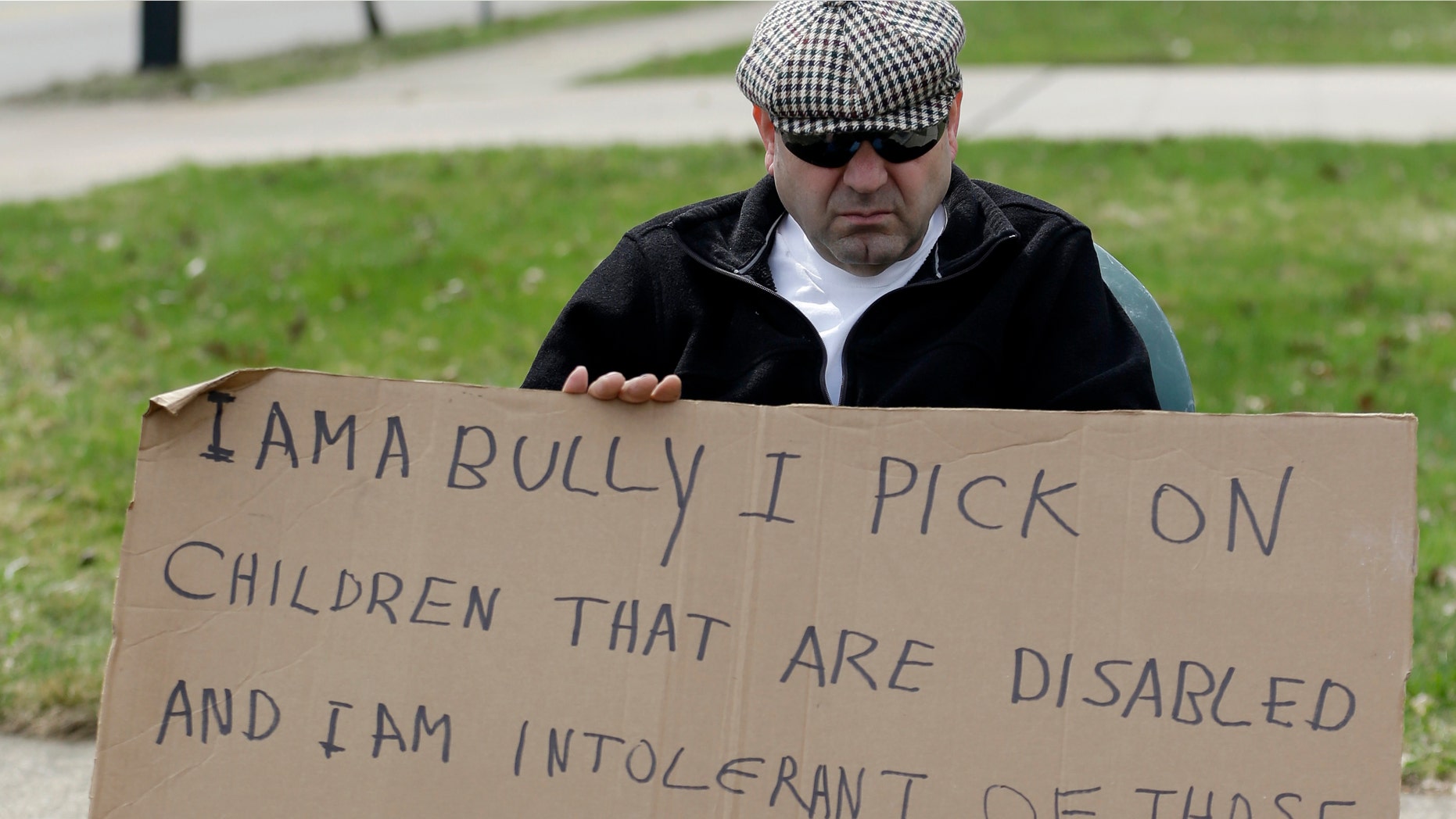 Following court orders, Edmond Aviv sits on a street corner holding a sign Sunday, April 13, 2014, in South Euclid, Ohio.