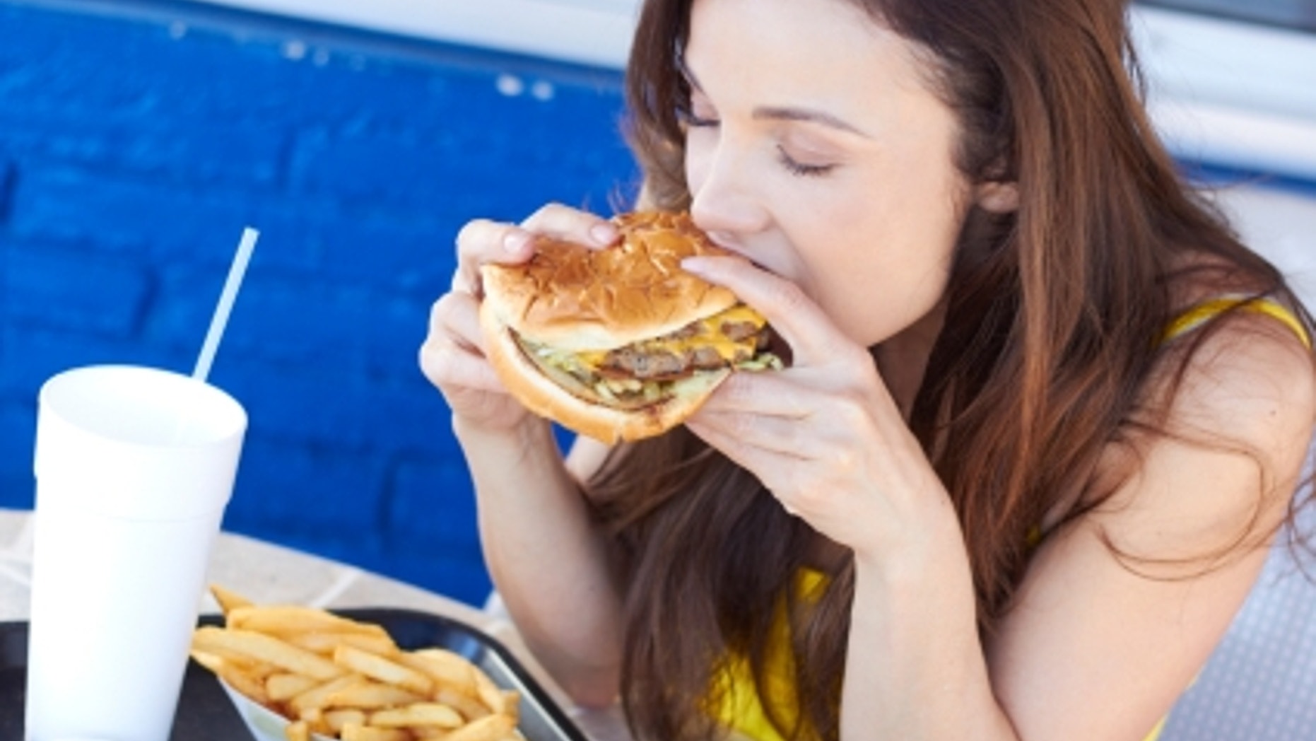 Beautiful young lady eating a tasty burger at an outdoor cafe. Horizontal Shot.