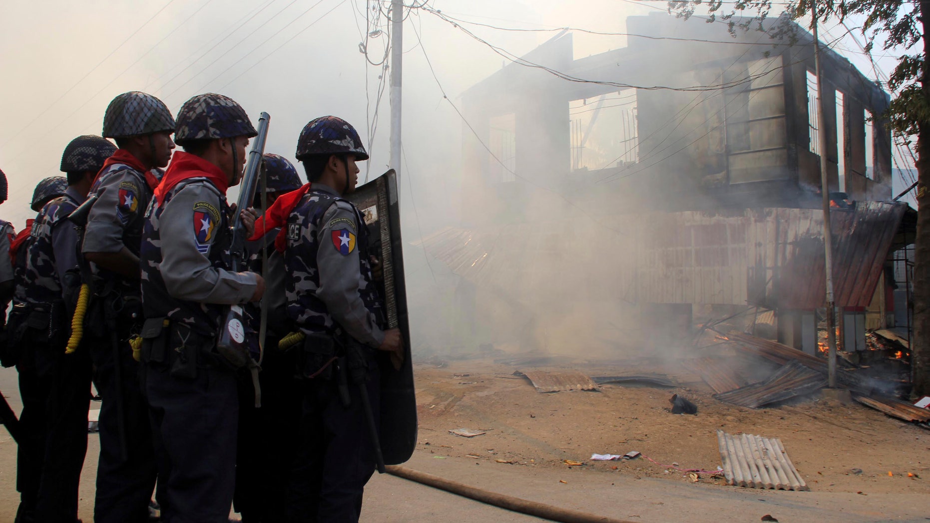 March. 21, 2013: This photo shows armed Burma police officers provide security around a smoldering building following ethnic unrest between Buddhists and Muslims in Meikhtila, Mandalay division, about 340 miles north of Yangon, Burma.