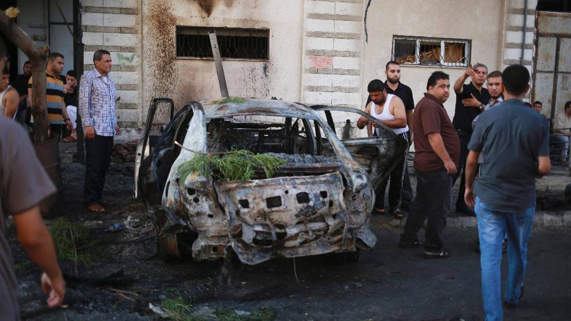 CORRECTS PHOTOGRAPHER'S NAME TO HASSAN MAHMOUD - Palestinians stand around a vehicle destroyed in blast in Gaza City on Sunday, July 19, 2015. At least four explosions rocked Gaza City early Sunday, targeting vehicles belonging to officials from Islamic factions, including the territory's Hamas rulers. There was no claim of responsibility, but speculation immediately centered on supporters of the Islamic State group, who have been battling with Hamas and other Islamic groups in the small coastal strip. (AP Photo/Hassan Mahmoud)