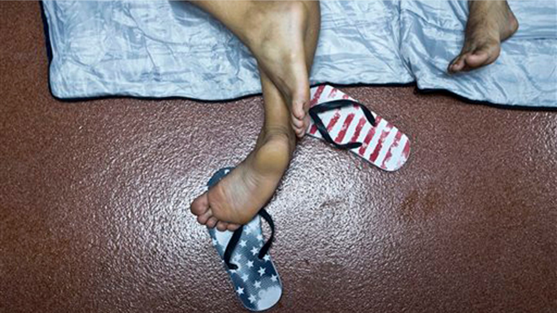FILE - In this Nov. 21, 2015 file photo, a Cuban migrant's feet rests on a pair of feet flip flops designed with stars and stripes, while resting inside the public restroom of the border control building in Penas Blancas, Costa Rica, border with Nicaragua. New U.S. statistics show nearly twice as many Cuban migrants reached the United States by foot and sea in the last three months of 2015 compared with the same period the year earlier, an exodus apparently fueled by the restoration of diplomatic relations between the former political foes. Department of Homeland Security figures show about 17,000 Cubans reached the United States from October through December. (AP Photo/Esteban Felix, File)