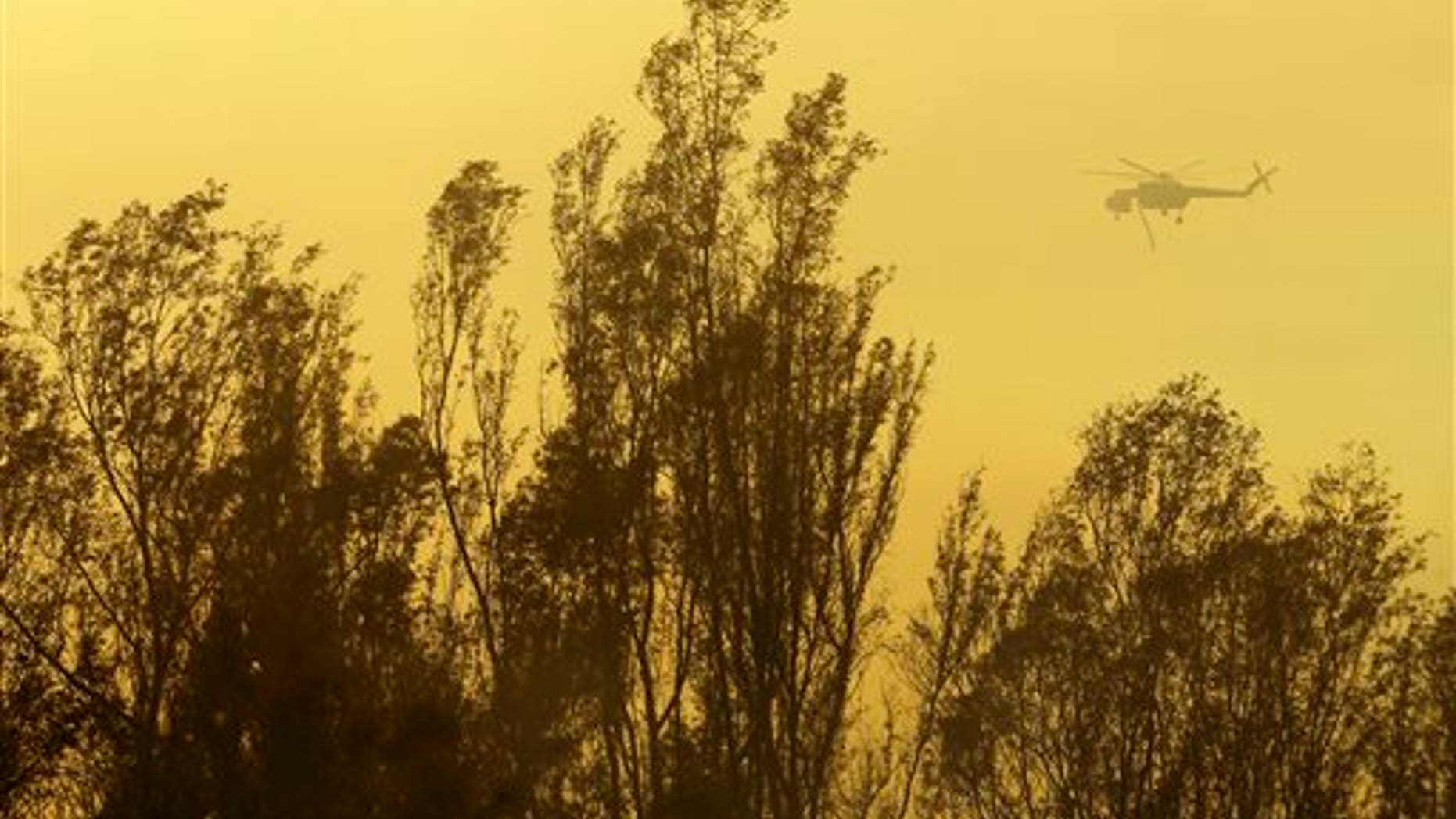 A helicopter transporting water flies over trees during a wildfire Thursday, May 15, 2014, in Escondido, Calif. One of the nine fires burning in San Diego County suddenly flared Thursday afternoon and burned close to homes, trigging thousands of new evacuation orders.(AP Photo/Gregory Bull)