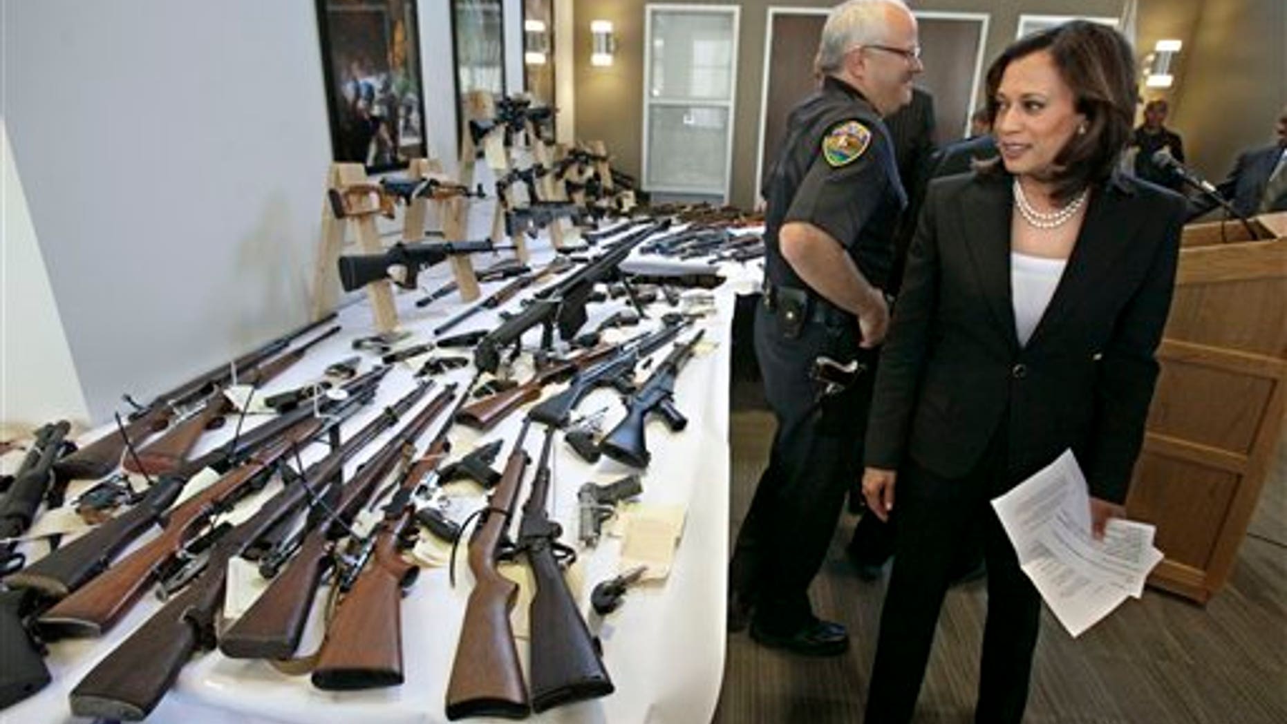 June 16: Attorney General Kamala Harris looks over some of the guns seized from individuals legally barred from possessing them following a news conference in Sacramento, Calif. In a recently concluded six-week sweep conducted by agents from the Department of Justice, 1,200 firearms were seized from individuals barred from owning them,including those determined to be mentally unstable and with active restraining orders against them.