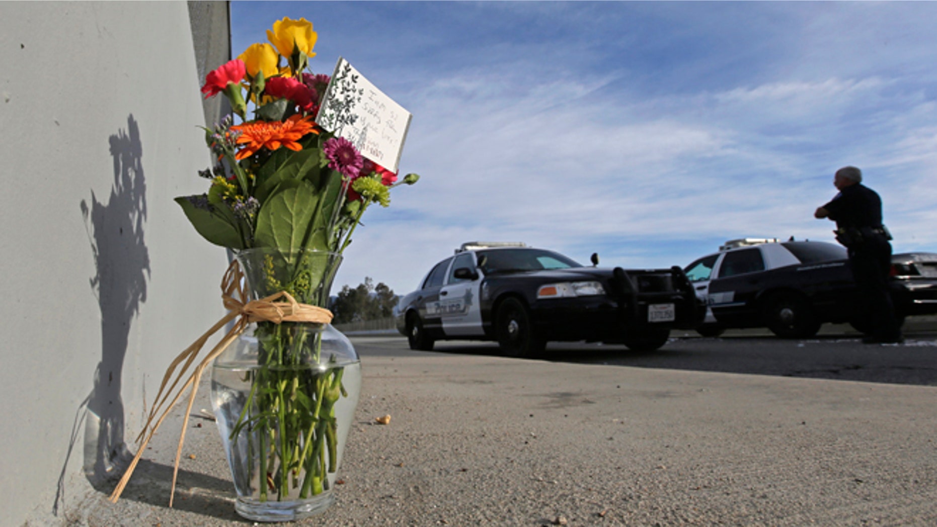 FILE - In this Dec. 3, 2015 file photo, flowers are left by the side of the road as a San Bernardino police officer blocks the road leading to the site of yesterday's mass shooting in San Bernardino, Calif. President Barack Obama plans to meet with families of victims of the mass shooting in San Bernardino, California, the White House said Wednesday. The meeting is set for Friday. Obama is adding the stop in Southern California to a long-scheduled trip to Hawaii for Christmas vacation. (AP Photo/Chris Carlson, File)