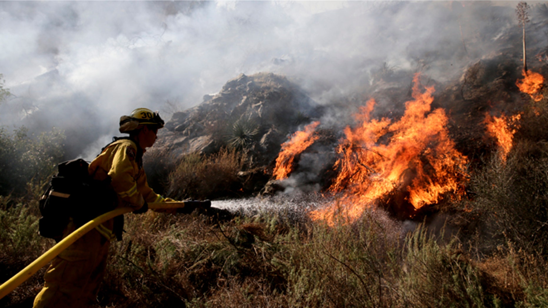 Firefighter Jeff Newby sprays water as he battles the Colby Fire on Friday, Jan. 17, 2014, near Azusa, Calif. Firefighters were chasing flare-ups Friday morning in a damaging wildfire that was largely tamed but kept thousands of people from their homes in the foothill suburbs northeast of Los Angeles.(AP Photo/Jae C. Hong)