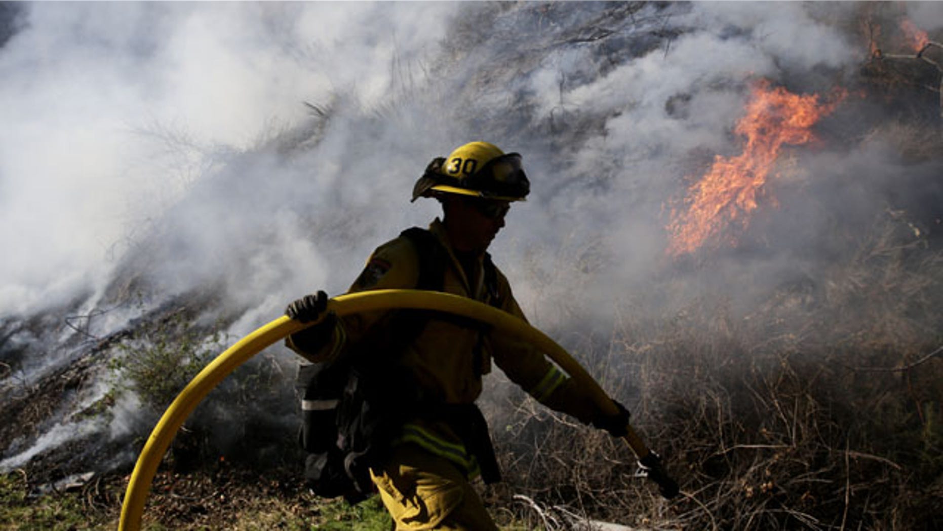 January 17, 2014: Firefighter Jeff Newby carries a water hose as he battles the Colby Fire near Azusa, Calif. (AP Photo)