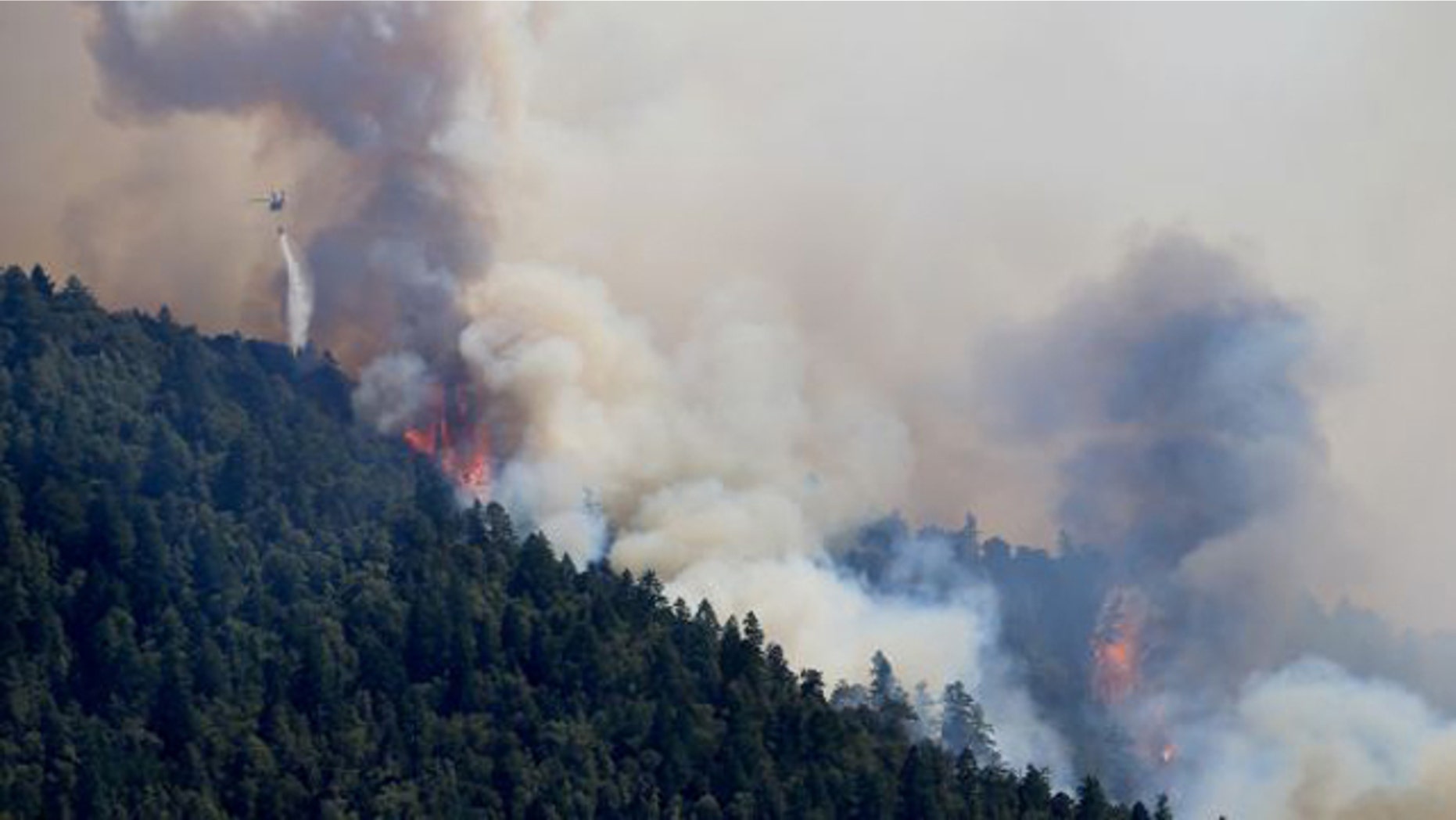 August 8, 2014: An Air National Guard helicopter makes a water drop as the Lodge Fire between Legget tand Laytonville, Calif., jumps the Eel River and moves upslope. (AP/Kent Porter)