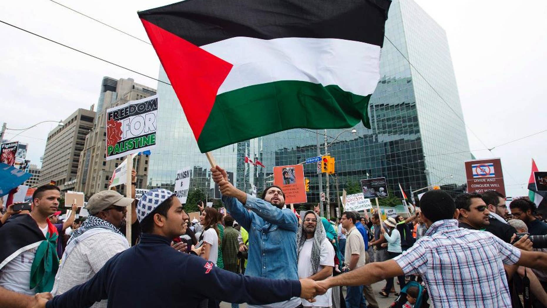 A Palestinian supporter waves a flag as others create a human barricade shielding them from opposing Israeli supporters during a rally protesting the war between Israel and Hamas members in the Gaza Strip in Toronto on Saturday, July 26, 2014. (AP Photo/The Canadian Press, Darren Calabrese)