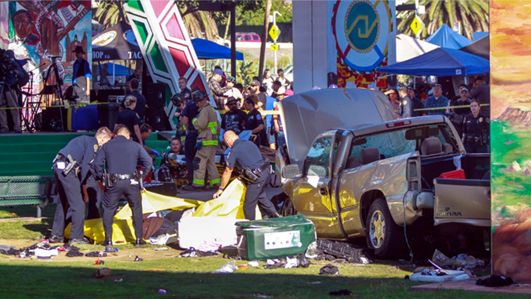 Police cover the bodies of people that were killed when a pickup truck landed on them after it flew off a ramp to the San Diego Coronado Bridge as paramedics prepare to put an injured man on a gurney, background, at Chicano Park in San Diego on Saturday, Oct. 15, 2016. Four people were killed and nine were injured on Saturday after an out-of-control pickup truck plunged off the San Diego-Coronado Bridge and plowed into crowd gathered at a festival below, authorities said. (Hayne Palmour IV/The San Diego Union-Tribune via AP)
