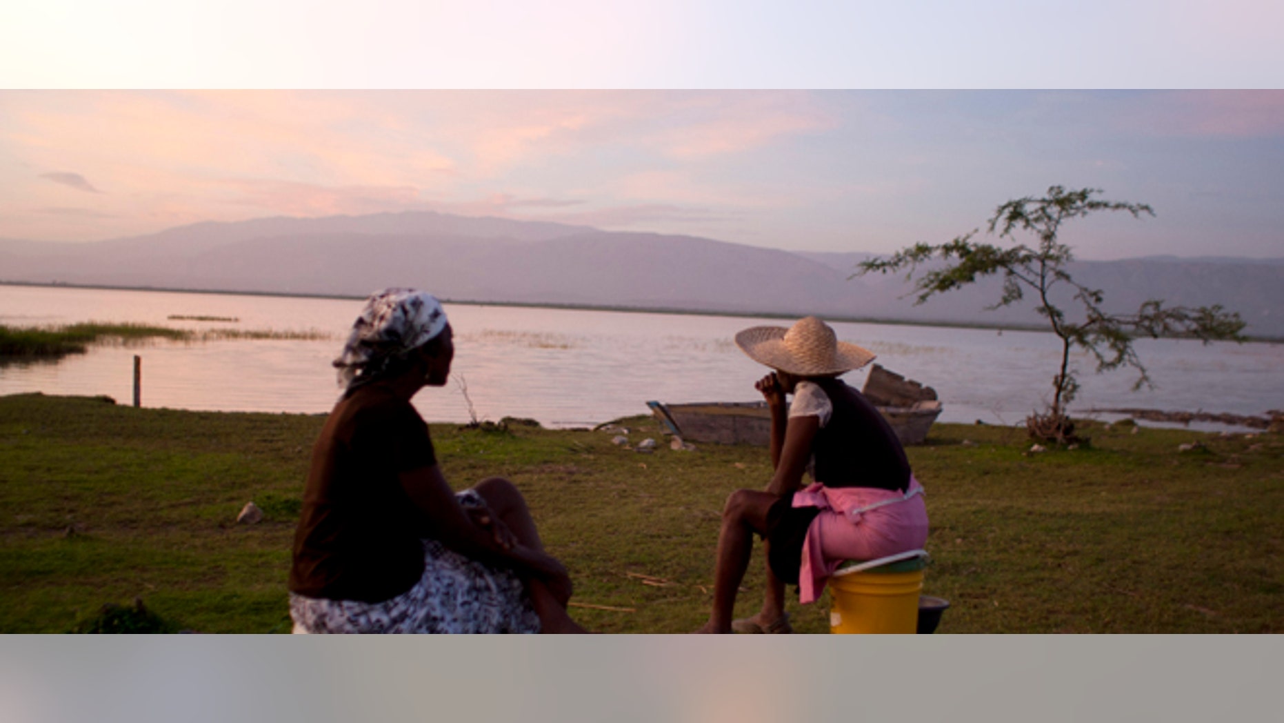 In this Aug. 22, 2013 photo, vendors Jacline Bienheme, left, and Marie Jolerme wait for fishermen to return on the shores of Lake Azuei in Thomazeau, Haiti. Experts are sounding a new alarm about the effects of climate change for parts of the Caribbean: the depletion of already strained drinking water throughout much of the region. (AP Photo/Dieu Nalio Chery)