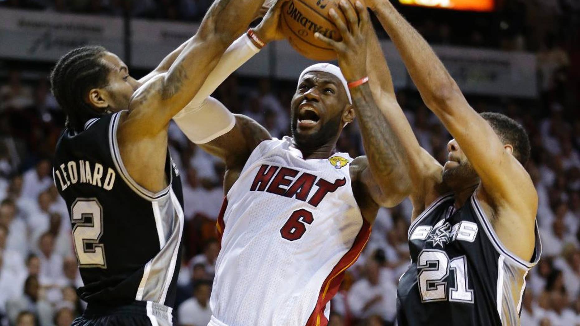 FILE - In this June 10, 2014, file photo, San Antonio Spurs forward Tim Duncan (21) and forward Kawhi Leonard (2) defend against Miami Heat forward LeBron James (6), during the first half in Game 3 of the NBA basketball finals in Miami. They've denied LeBron James winning two NBA titles, and in last year's Finals the Spurs dismantled the Heat, a beatdown that may have hastened the superstar's decision to re-sign with the Cavaliers. On Wednesday, Nov. 19, James faces his nemesis for the first time since June. By(AP Photo/Wilfredo Lee, File)