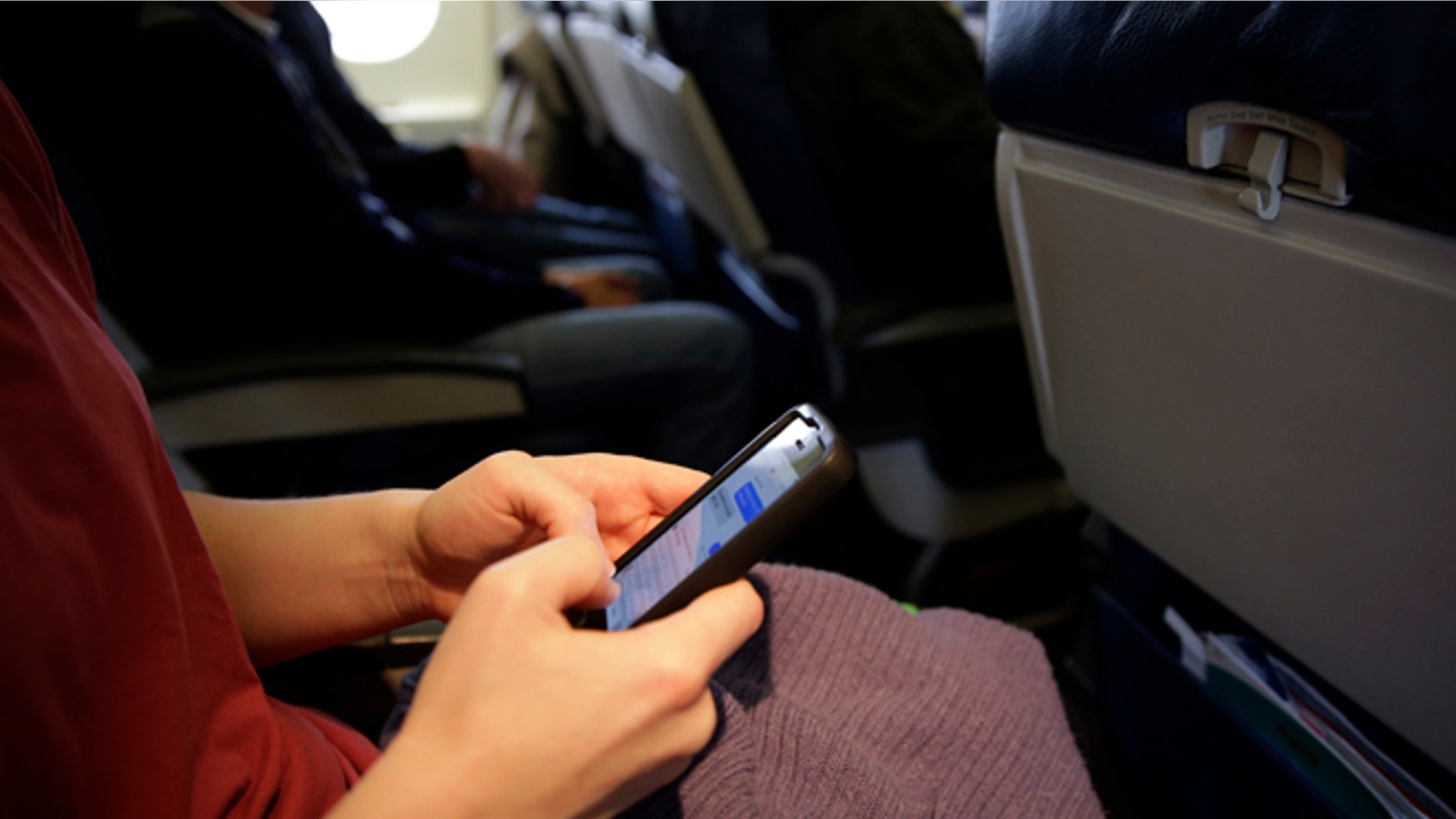 FILE - This Oct. 31, 2013 file photo shows a plane passenger checking her cell phone before a flight in Boston. While one government agency considers allowing cellphone calls on passenger planes, another now wants to ban them. The Transportation Department signals that it wants to impose a ban on inflight cellphone calls, just two months after the Federal Communications Commission (FCC) voted to pursue lifting the current ban. The FCC regulates wireless communications, while the transportation department regulates issues affecting airline passengers. (AP Photo/Matt Slocum, File)