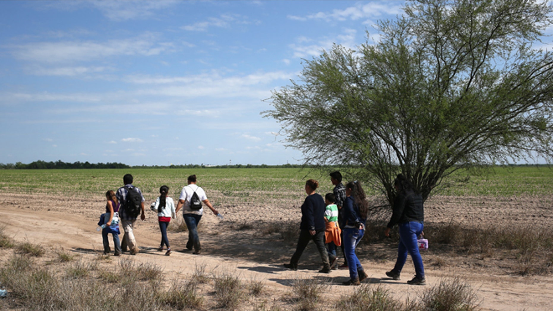 Central American families walk through the countryside after crossing from Mexico on April 14, 2016 in Roma, Texas.