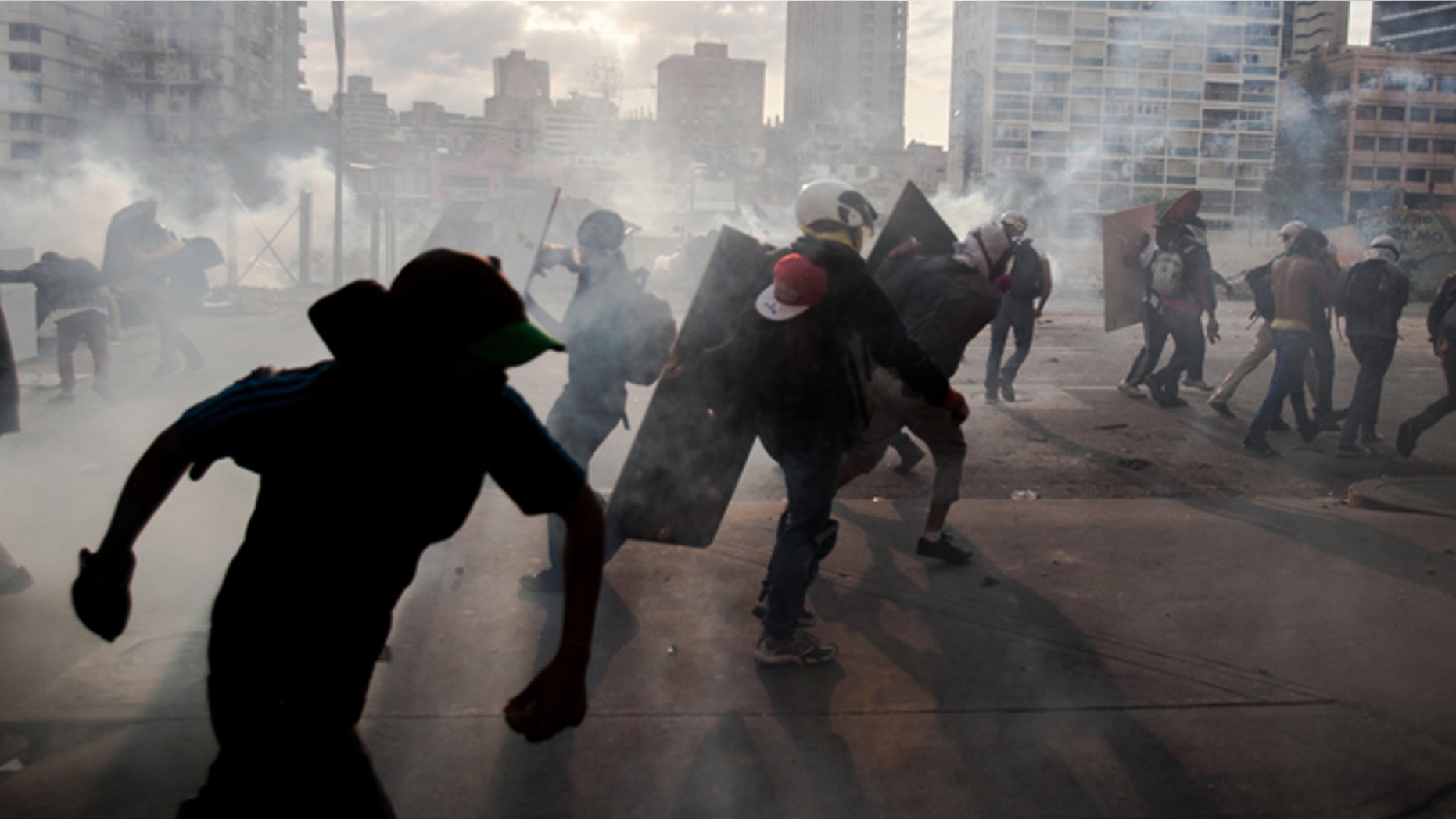 Demonstrators take cover from teargas fired by the police during clashes in an anti-government protest in Caracas, Venezuela, Monday, March 10, 2014. The Venezuelan government and opposition appear to have reached a stalemate, in which street protests continue almost daily while the opposition sits out a peace process it calls farcical. (AP Photo/Alejandro Cegarra)