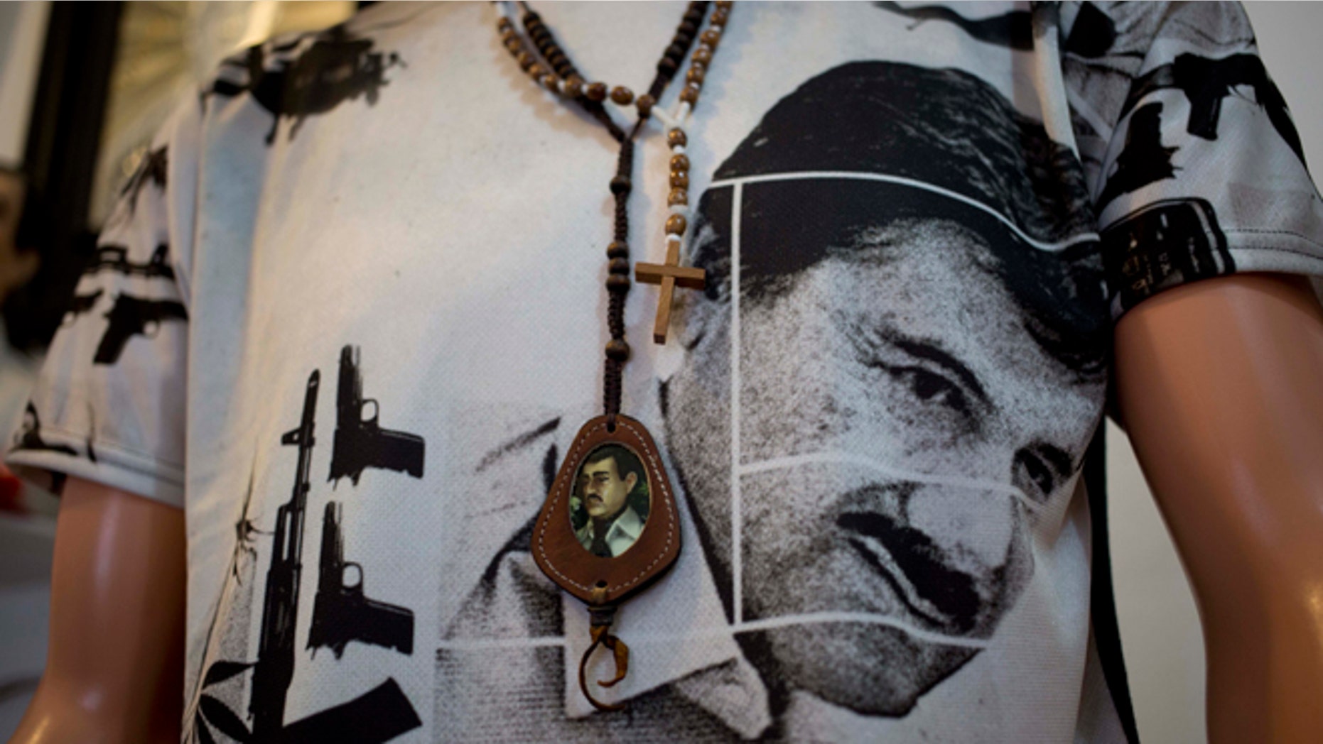 A T-shirt of fugitive Mexican drug lord Joaquin "El Chapo" Guzman covers a mannequin representing Jesus Malverde, known in Mexico as the "Saint" of drug traffickers, inside the shrine of a faith healer in Mexico City, Friday, Oct. 16, 2015. The government is offering a reward of 60 million pesos, or about $3.5 million dollars, for Guzman's recapture after he made his second escape from a maximum security prison through an underground tunnel in 2015. (AP Photo/Eduardo Verdugo)